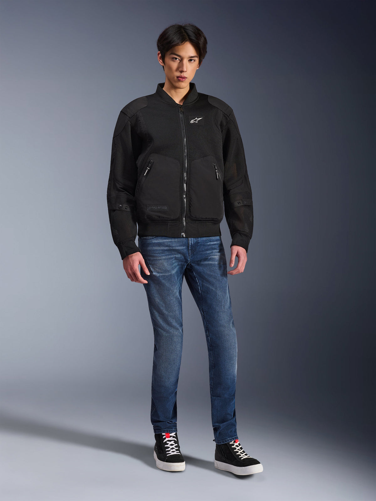 Kurtka Alpinestars Flight Air, czarna, miejska kurtka motocyklowa typu bomber z panelami z siatki 3D i białym logo na piersi, model w niebieskich jeansach i czarnych sneakersach, nowoczesna odzież motocyklowa