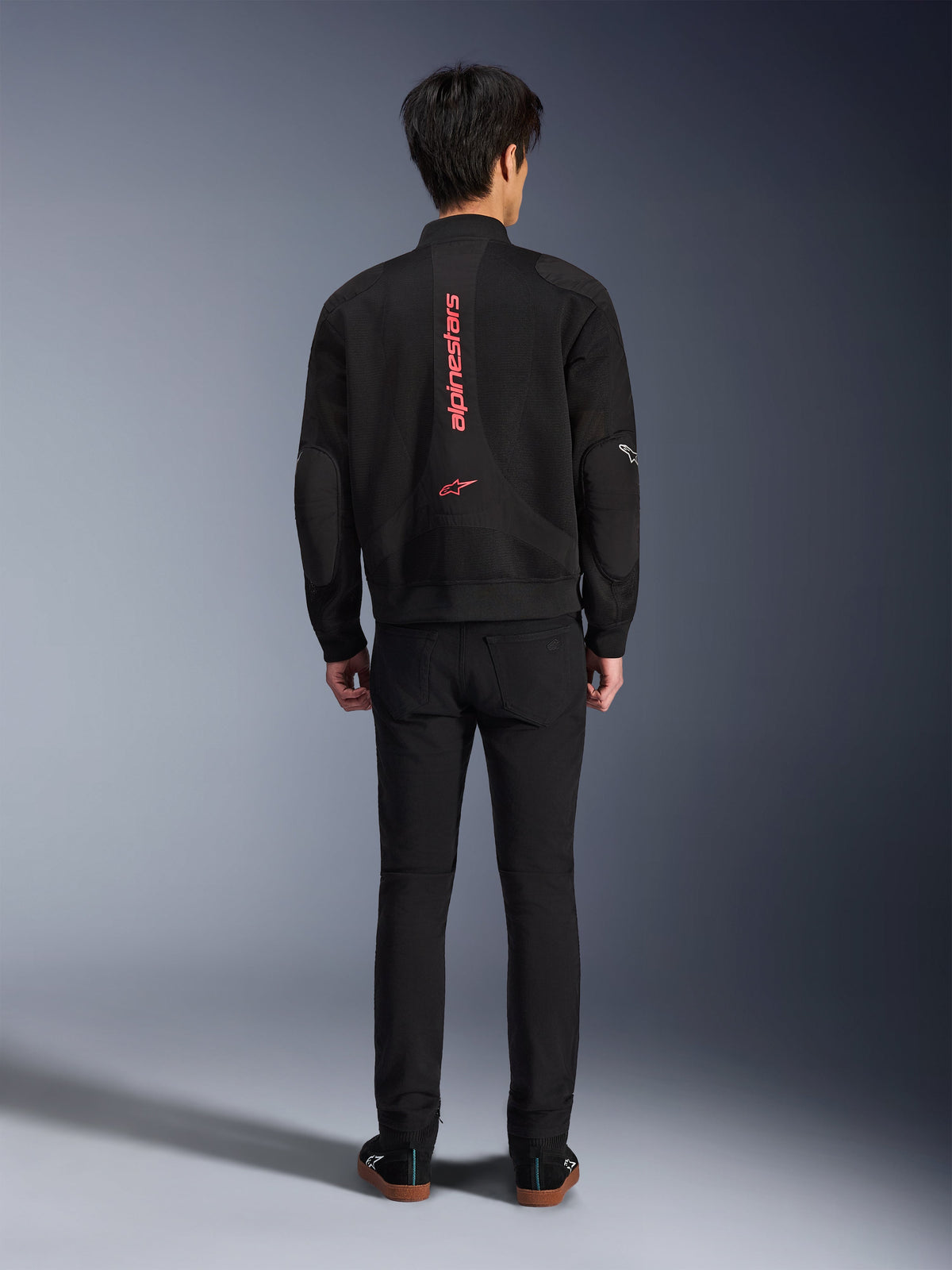 Kurtka Alpinestars Flight Air w kolorze Black Bright Red, widok z tyłu miejskiej kurtki motocyklowej typu bomber, z pionowym czerwonym napisem i logo Alpinestars na plecach, lekka konstrukcja z siatki 3D, zestawiona z czarnymi spodniami dla nowoczesnego wyglądu.
