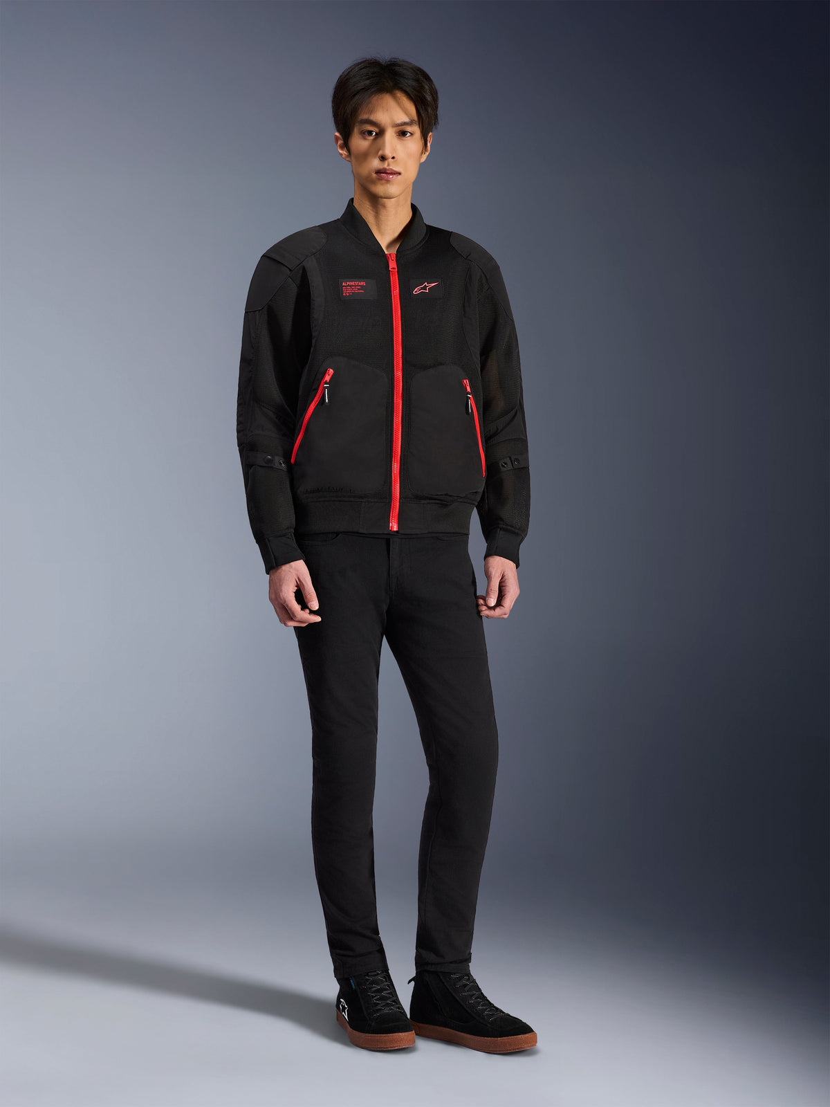 Alpinestars Flight Air Jacket w kolorze Black Bright Red, miejska kurtka motocyklowa w stylu bomber z panelami z siatki 3D i jaskrawymi czerwonymi zamkami, noszona przez modela z czarnymi spodniami slim-fit i czarnymi sneakersami, współczesna odzież motocyklowa inspirowana stylem ulicznym