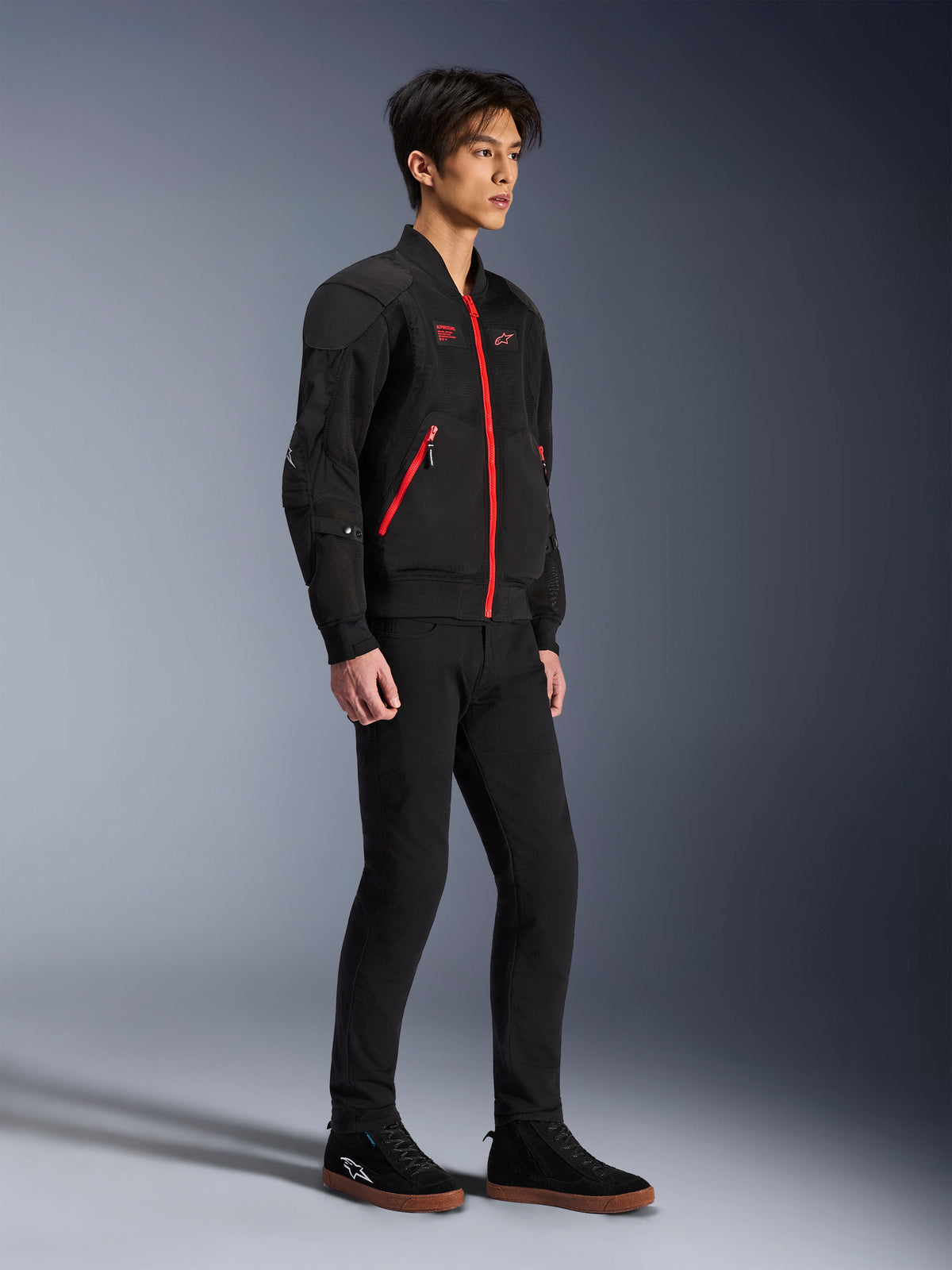 Alpinestars Flight Air Jacket, czarno-czerwona, miejska kurtka motocyklowa typu bomber prezentowana przez modela, panele z siatki 3D i kontrastujące czerwone zamki, w zestawie z czarnymi spodniami i codziennymi butami motocyklowymi, nowoczesna odzież ochronna inspirowana stylem ulicznym
