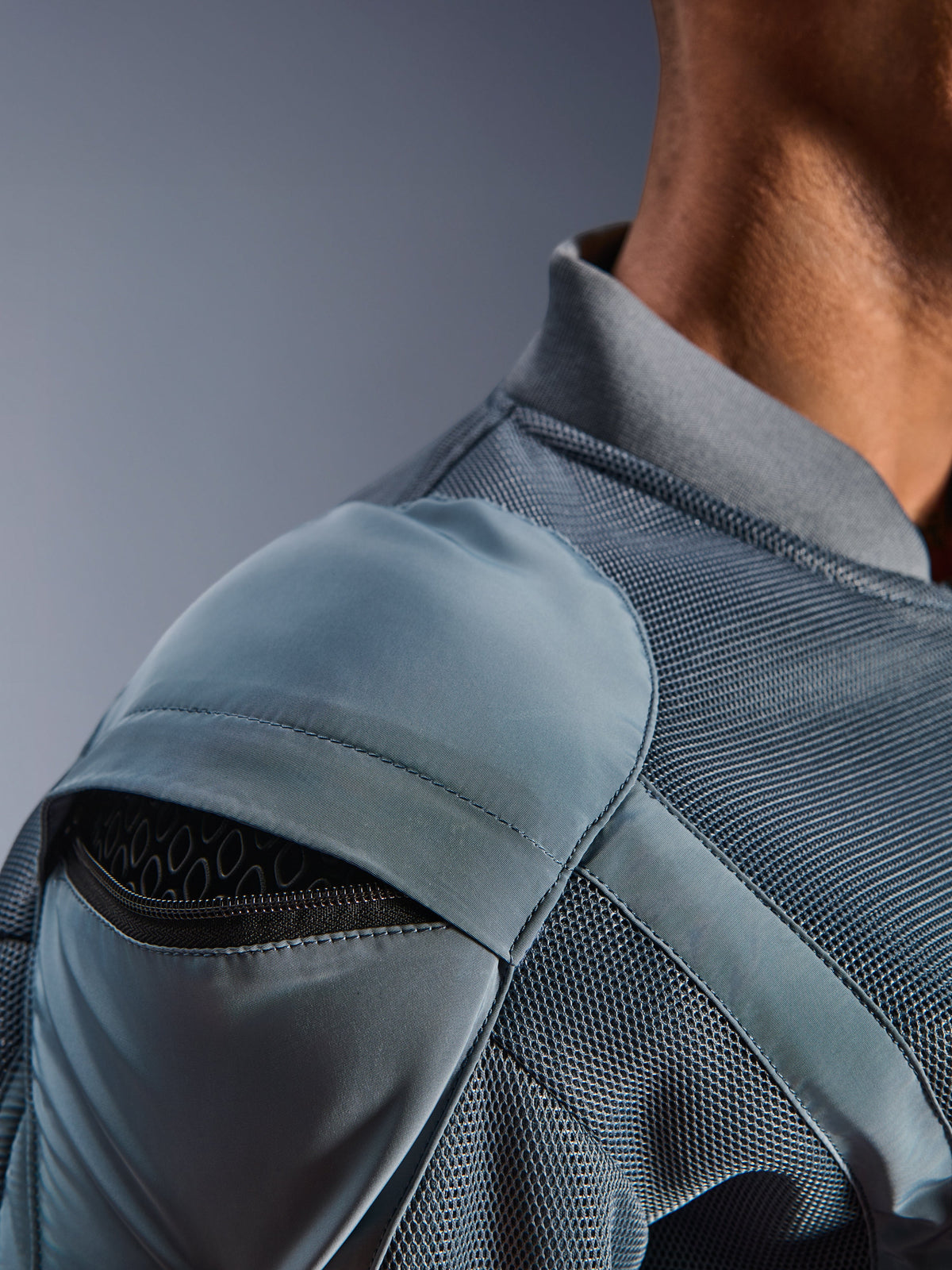 Zbliżenie na kurtkę Alpinestars Flight Air w kolorze Storm Gray, prezentujące zewnętrzną kieszeń na ochraniacz ramienia z widocznym pancerzem o strukturze plastra miodu, panele wentylacyjne z siatki 3D i żebrowany kołnierzyk do technicznej jazdy miejskiej