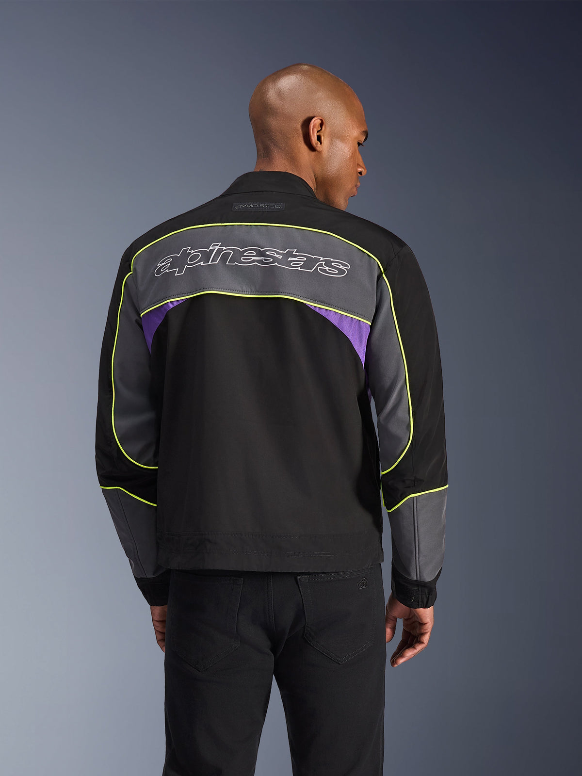 Alpinestars Unite Jacket, miejska kurtka motocyklowa, Black Asphalt Violet, widok z tyłu z szarymi panelami i fioletowymi akcentami, limonkowo-żółte lamówki, duży logotyp Alpinestars na plecach, minimalistyczny design streetwearowy