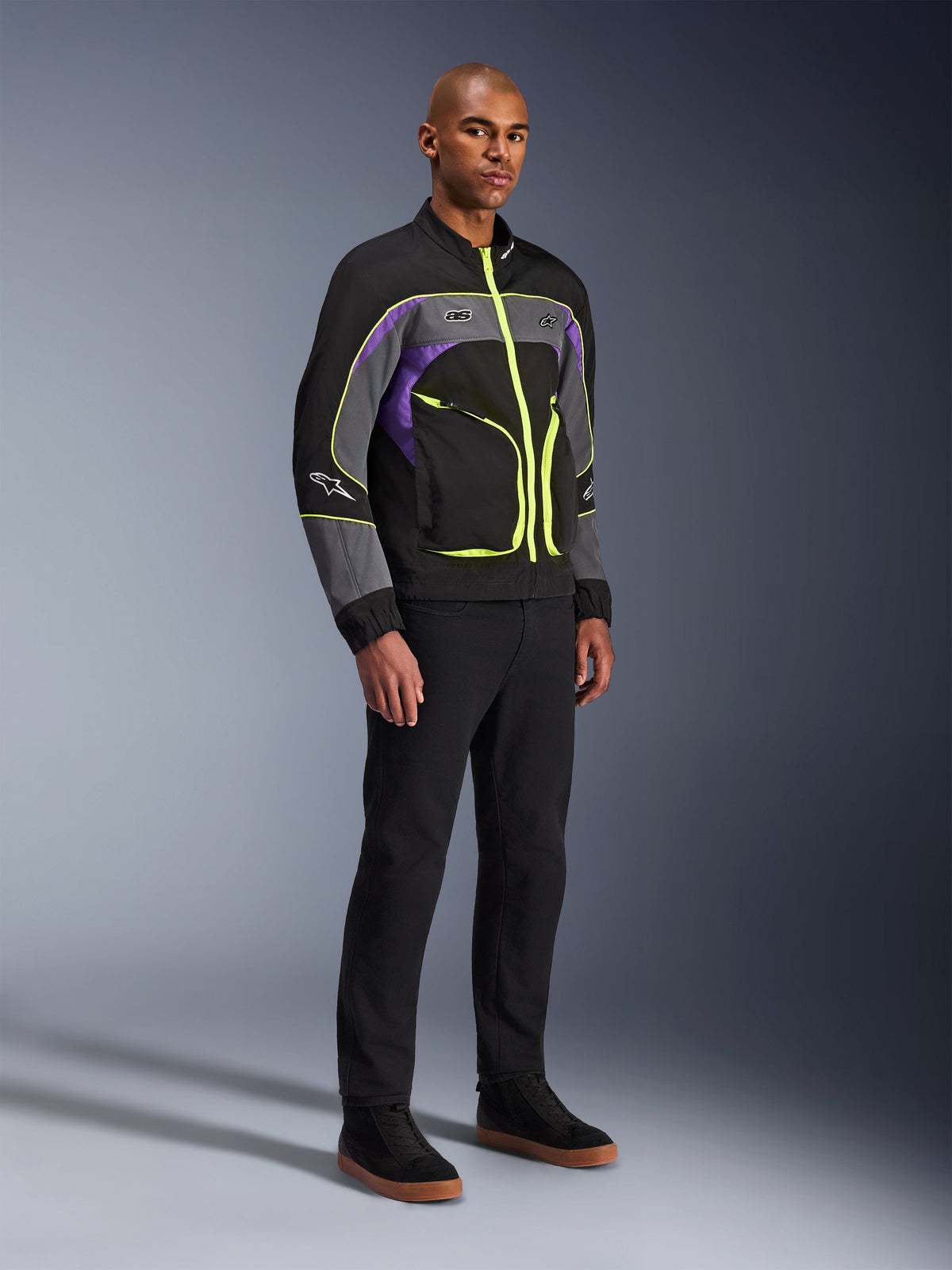 Kurtka Alpinestars Unite, miejska kurtka motocyklowa, Black Asphalt Violet z neonowożółtymi akcentami, noszona przez modela z czarnymi spodniami i sneakersami, współczesny styl streetwear do jazdy miejskiej