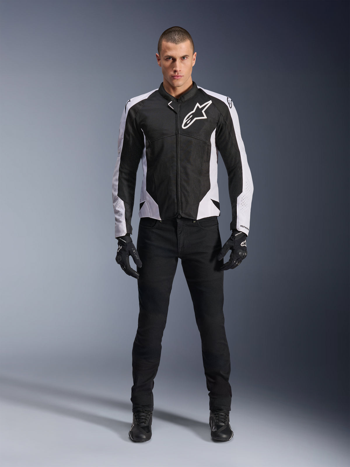 Kurtka Alpinestars Viper Air V4, czarno-biała kurtka motocyklowa z dużym białym logo na klatce piersiowej, noszona przez modela w czarnych spodniach i rękawicach, panele siatkowe zapewniające wentylację, sportowa odzież do jazdy szosowej