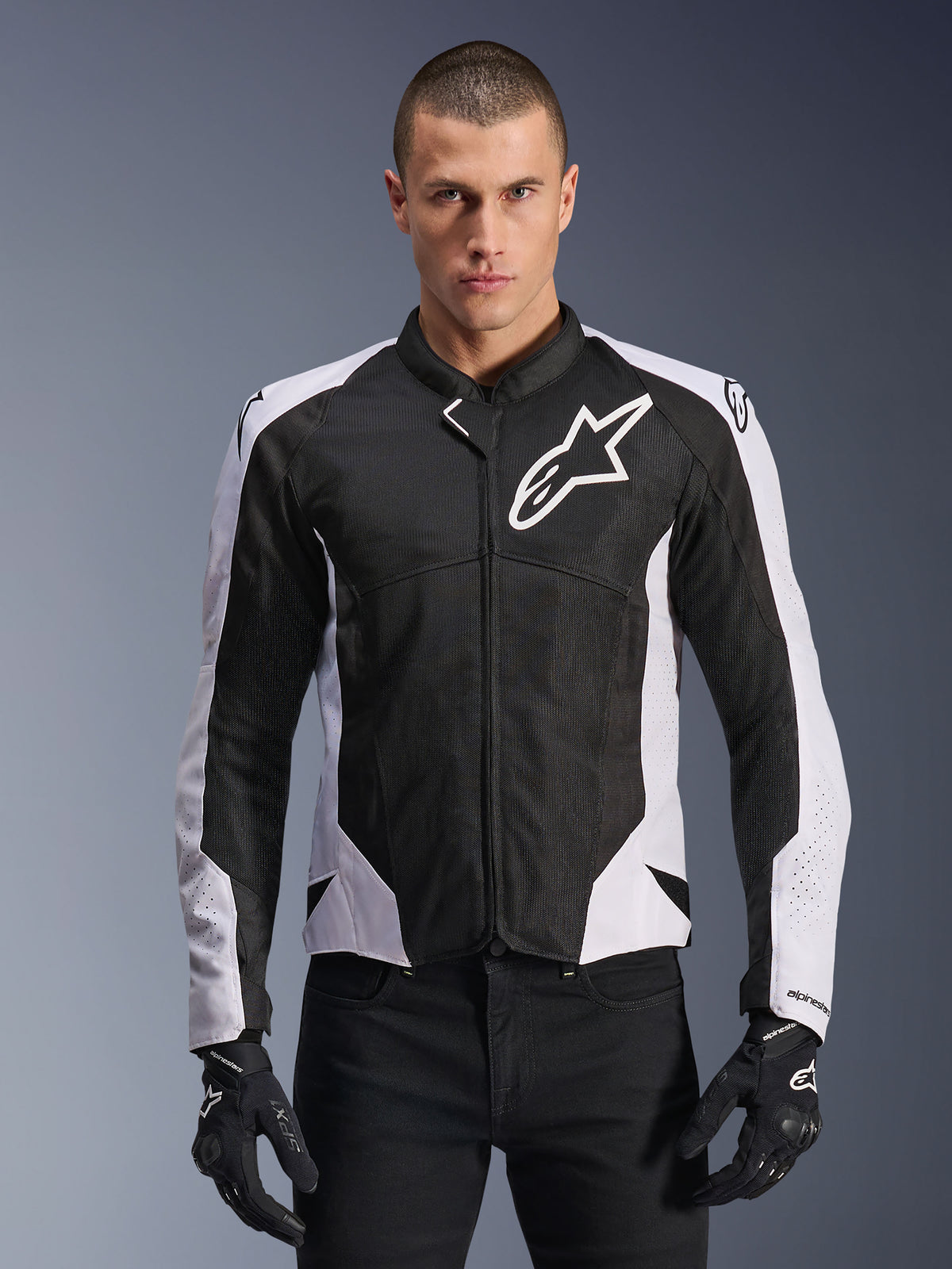 Alpinestars Viper Air V4 Jacket, motocyklowa kurtka wyścigowa, czarno-biała, noszona przez motocyklistę, konstrukcja z technicznej siatki i materiału tekstylnego z białymi panelami na ramionach, wyraźne logo gwiazdy na klatce piersiowej, sportowy design, w zestawieniu z czarnymi rękawicami motocyklowymi