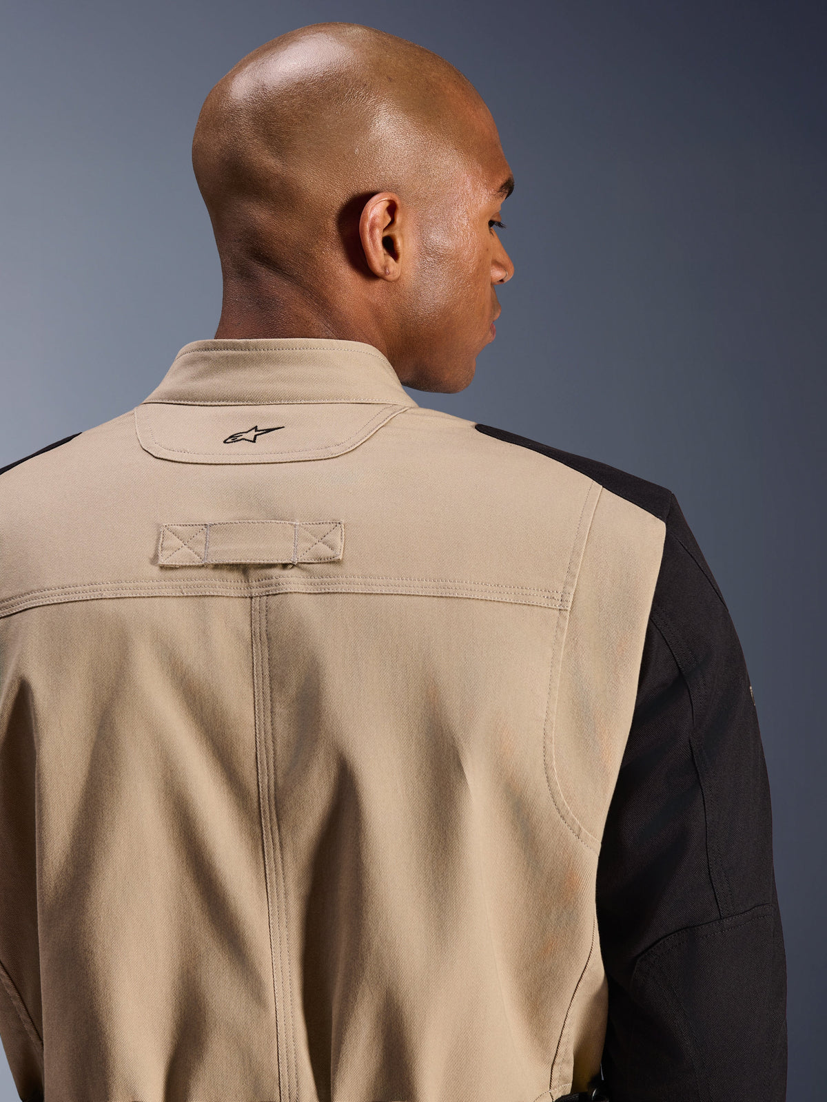 Alpinestars Dice Jacket, miejska kurtka motocyklowa, piaskowa i czarna, zbliżenie na detale kołnierza i ramienia z tyłu, z haftowanym logo, wytrzymała konstrukcja z diagonalnej polibawełny, miejski styl odzieży roboczej