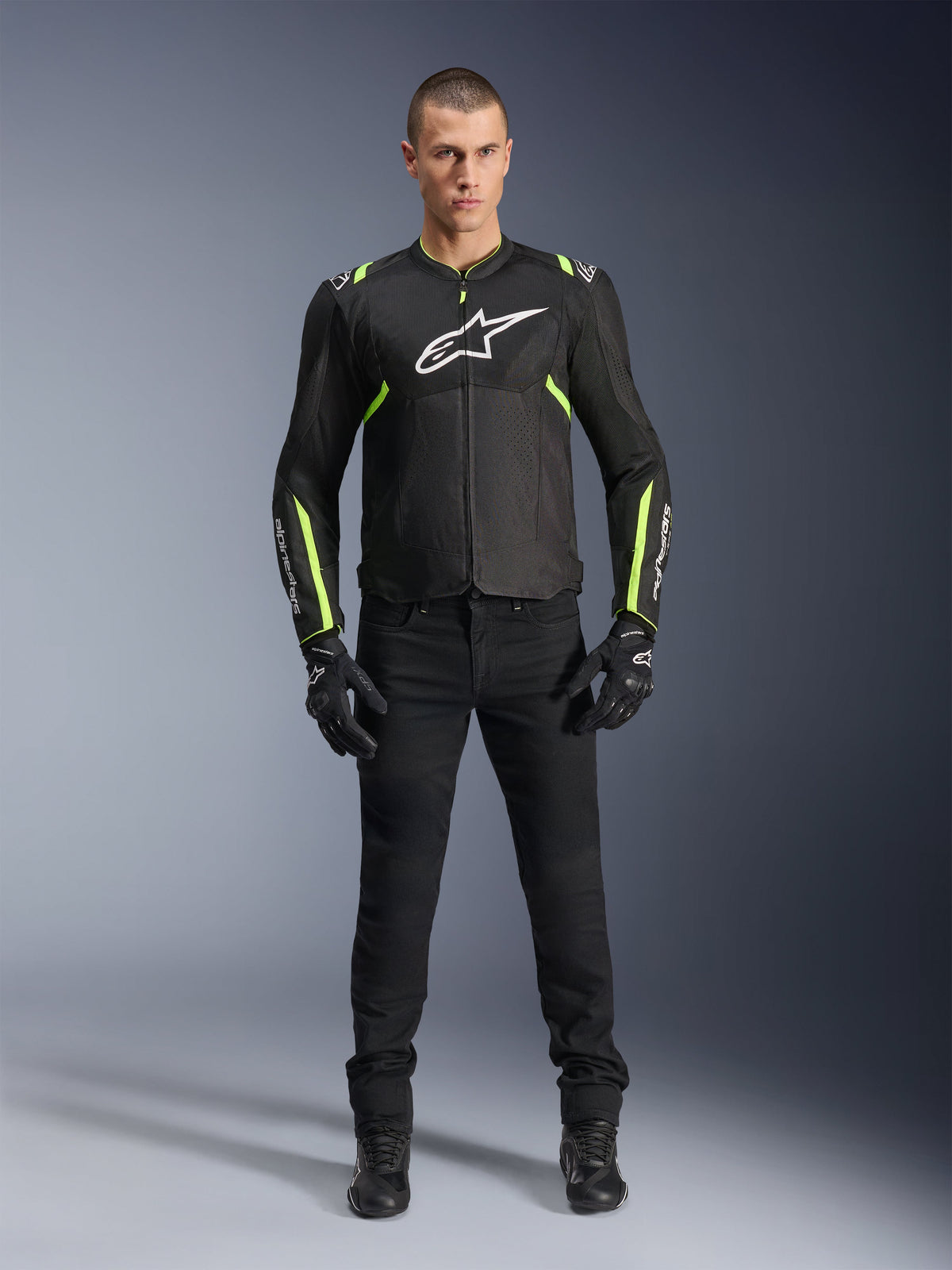 Kurtka Alpinestars T-Sps Air V2, czarna i żółta fluo, tekstylna kurtka motocyklowa z panelami z siatki, prezentowana przez modela w czarnych spodniach i rękawicach, białe logo Alpinestars na piersi, miejska sportowa odzież motocyklowa