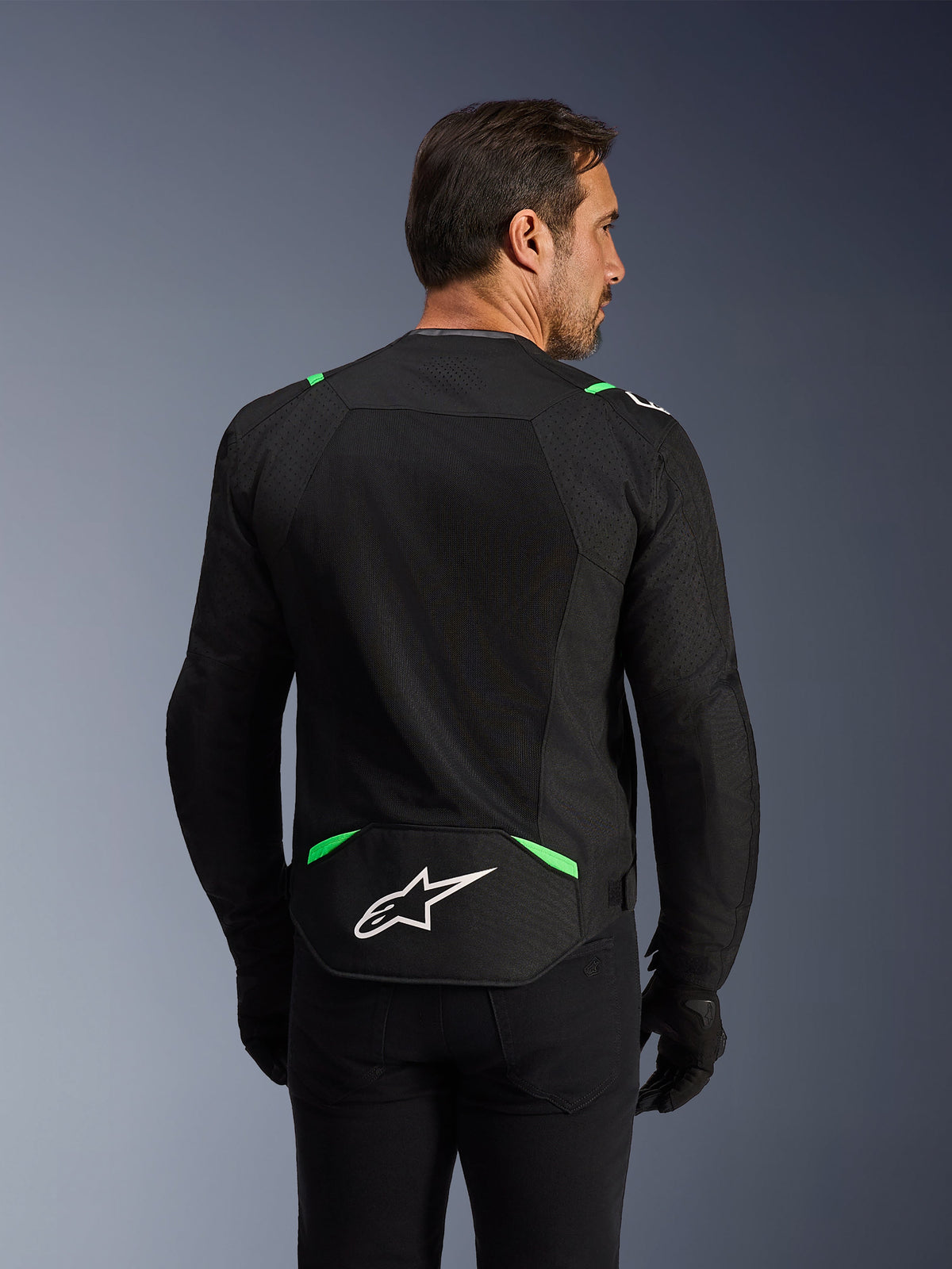 Kurtka Alpinestars T-SPS Air V2, tekstylna kurtka motocyklowa, czarna z neonowo-zielonymi elementami, widok z tyłu z dużymi panelami z siatki technicznej dla wentylacji, białe logo Alpinestars w dolnej części pleców, sportowy ergonomiczny krój do jazdy miejskiej