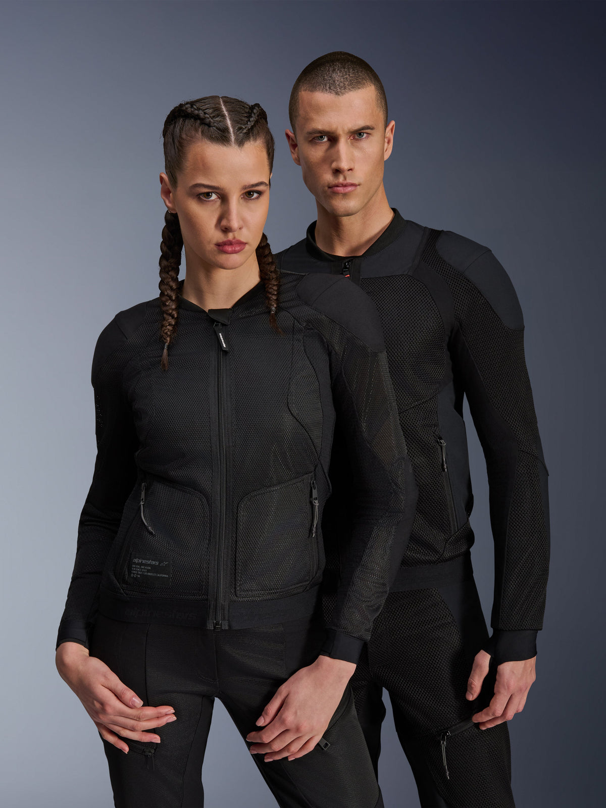 Alpinestars Troop-Air Pro Jacket, czarne techniczne kurtki motocyklowe z pancerzem noszone przez modela i modelkę, oddychające panele z siatki i zintegrowana ochrona, miejska odzież motocyklowa zaprojektowana do jazdy w ciepłe dni