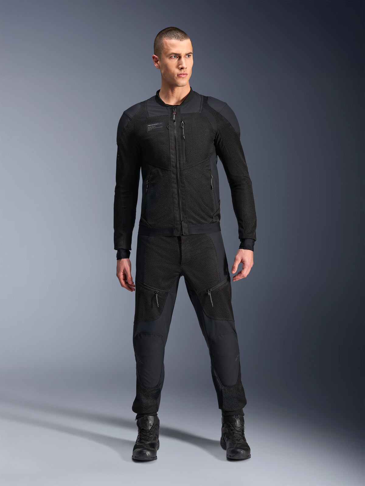 Alpinestars Troop-Air Pro Jacket, czarna techniczna kurtka motocyklowa z pancerzem, panele z siatki i zamki z przodu, noszona z pasującymi czarnymi spodniami i butami motocyklowymi, wysokiej klasy miejska odzież szosowa