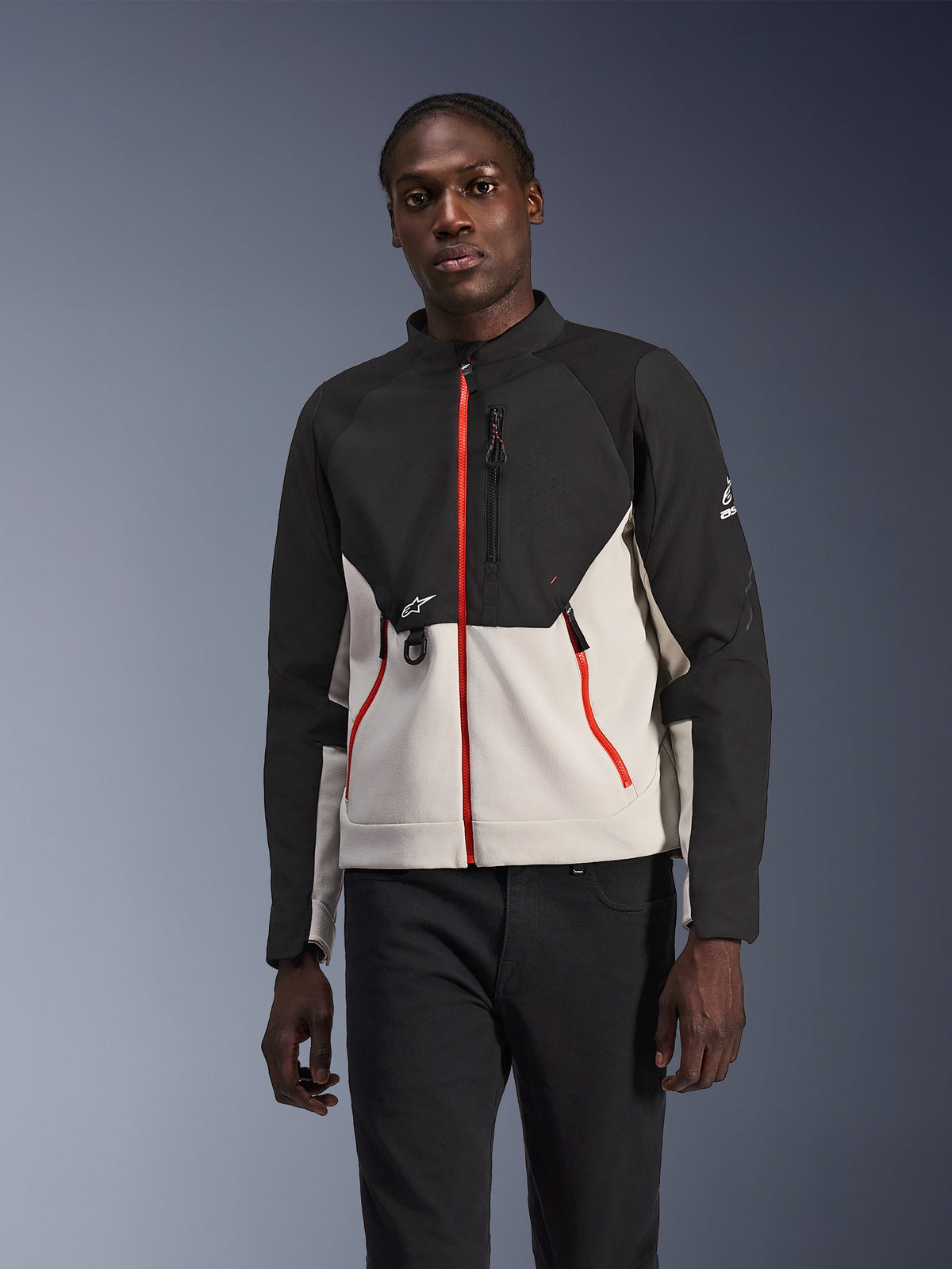 Kurtka Alpinestars Provoke, miejska kurtka motocyklowa, czarno-jasnoszara z jaskrawoczerwonymi zamkami błyskawicznymi, wysoki kołnierz, z detalami logo na piersi i rękawie, nowoczesny design ochronny do jazdy miejskiej prezentowany przez modela