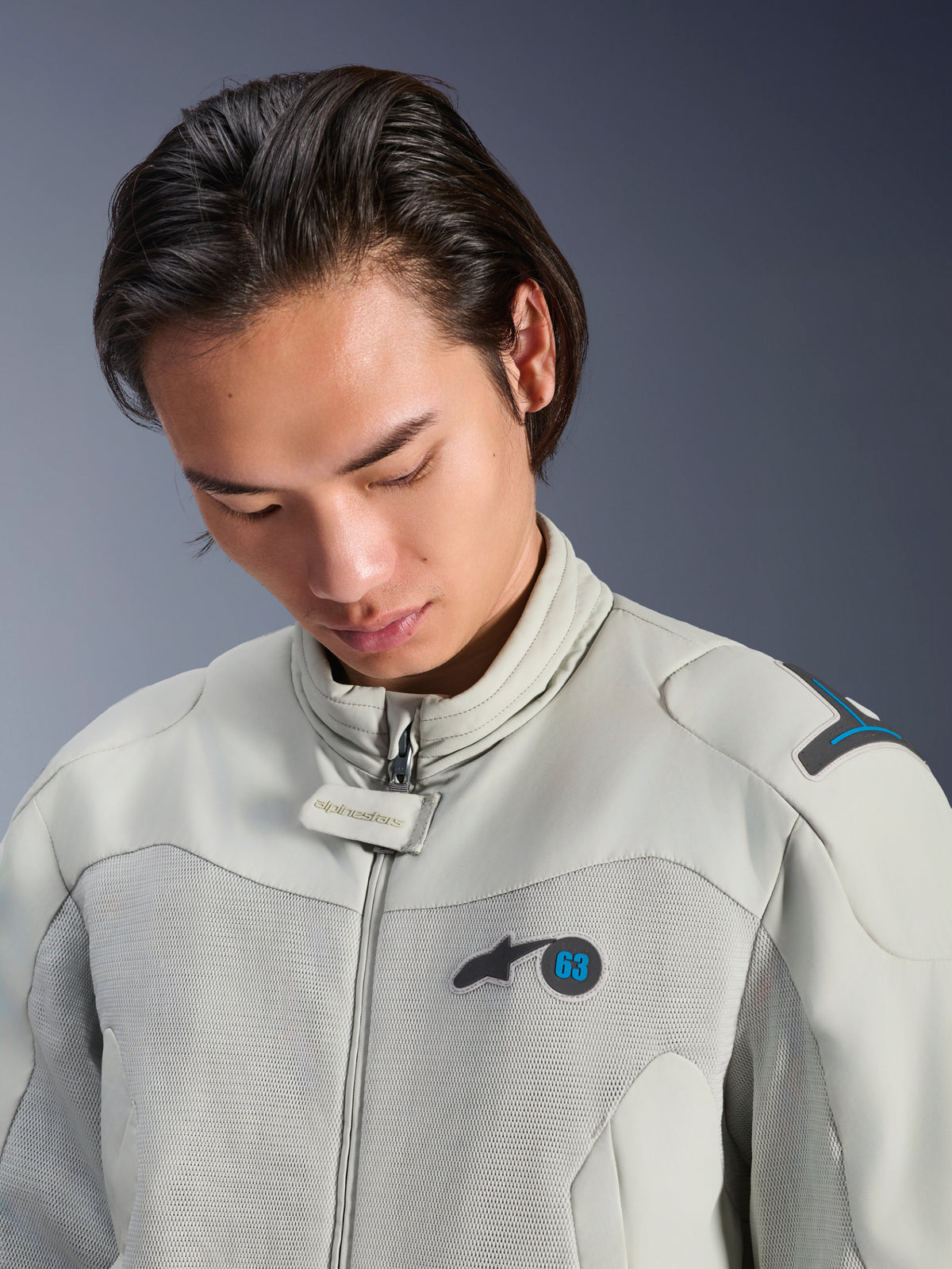 Męski model w kurtce Alpinestars Circal-1 Air Jacket w kolorze Metal Gray z akcentami Methyl Blue, zbliżenie podkreślające kołnierz, siateczkowe panele na klatce piersiowej i minimalistyczne logo, zrównoważona miejska odzież motocyklowa.