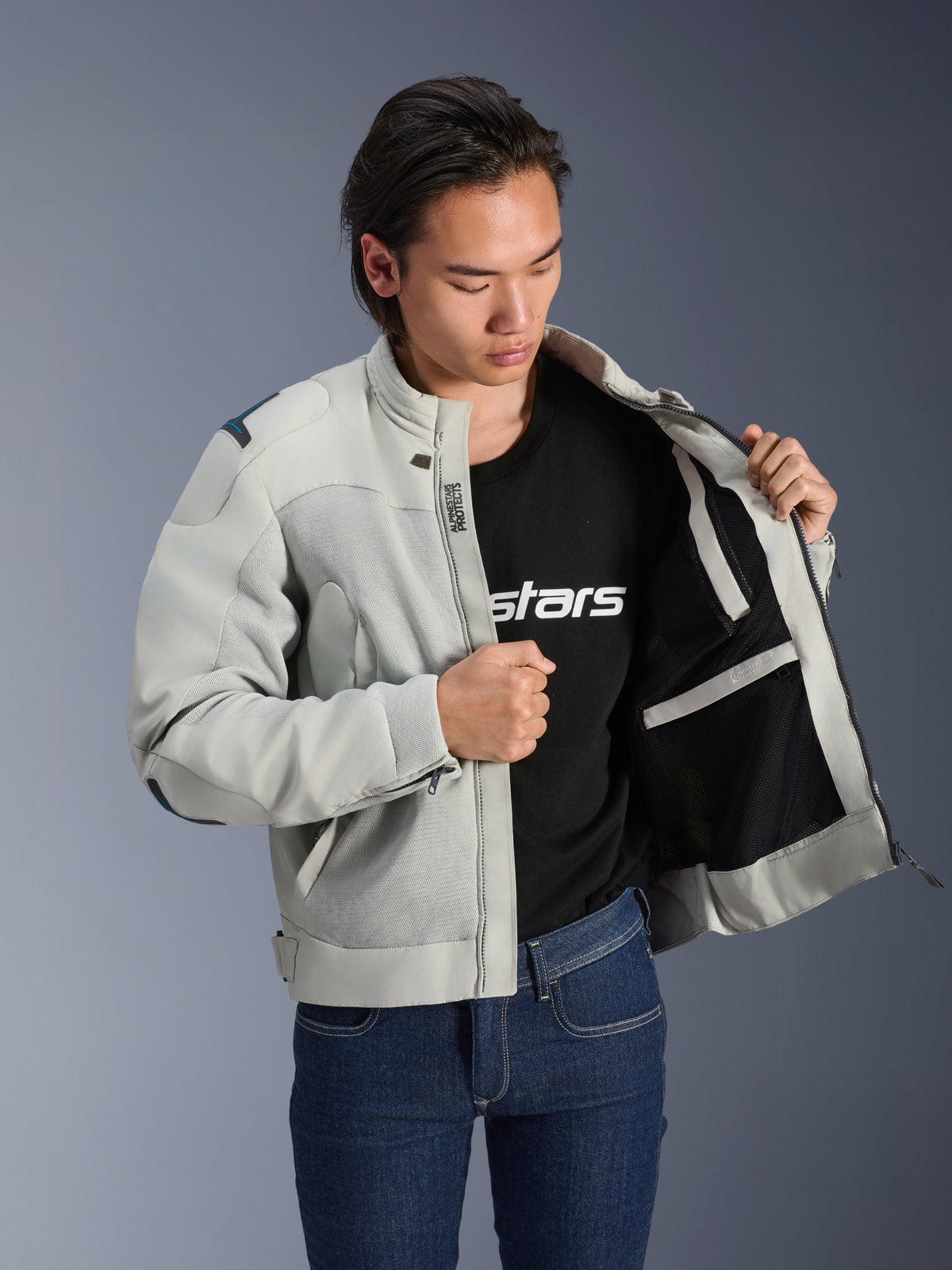 Kurtka Alpinestars Circal-1 Air, kolor Metal Gray, rozpięta, ukazująca wewnętrzną podszewkę z siateczki i detale kieszeni, noszona przez modela w czarnym t-shircie z logo i niebieskich jeansach, miejski styl motocyklowy