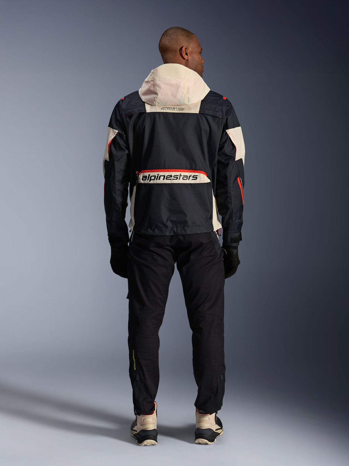 Alpinestars Mogress Air, męska kurtka motocyklowa, czarna i pomarańczowa, kremowy kaptur, miejski styl, widok z tyłu.