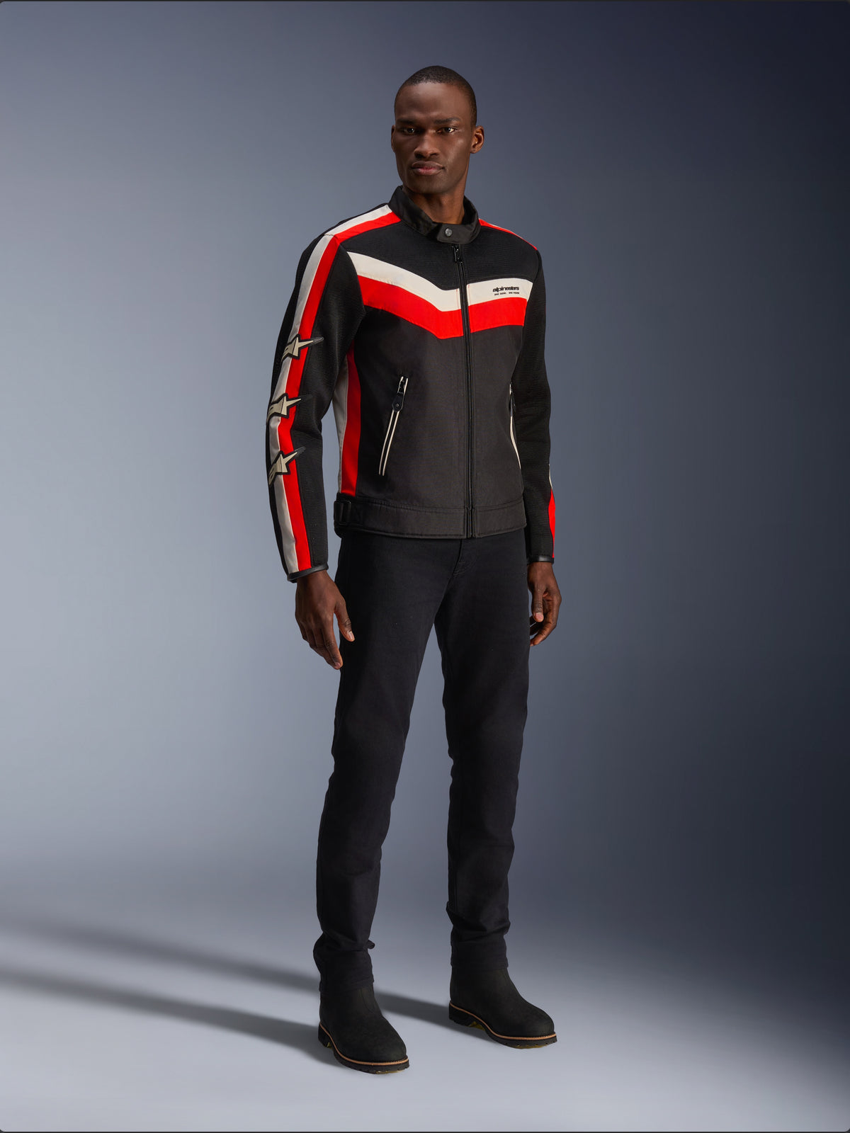Alpinestars T-Dyno Air Jacket, czarna z jaskrawoczerwonym i ecru, męska tekstylna kurtka motocyklowa z panelami z siatki 3D, czerwone i białe pasy w kształcie szewronu na klatce piersiowej oraz logo gwiazdy na rękawach, noszona przez modela w czarnych spodniach i butach.
