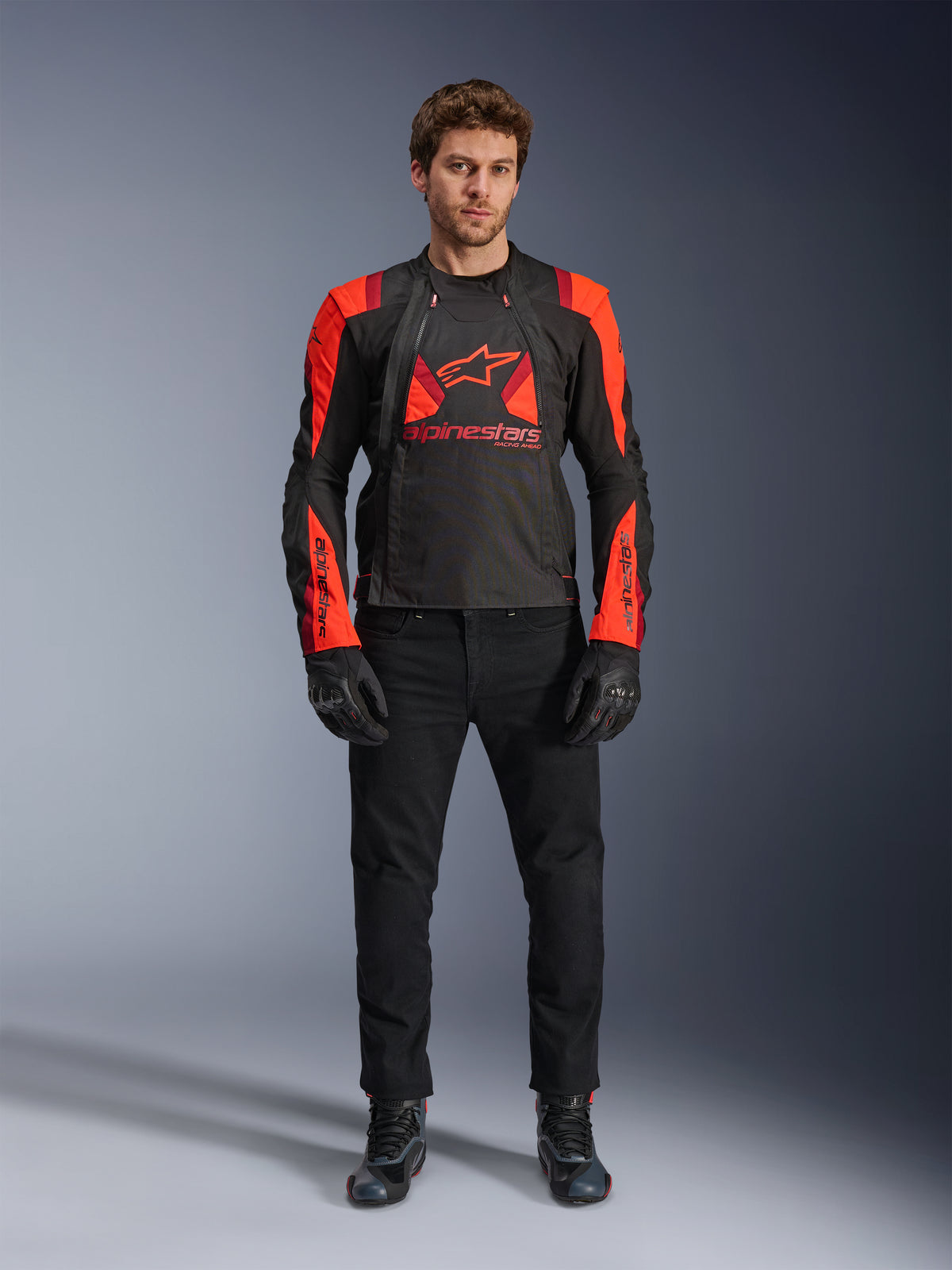 Kurtka Alpinestars T-Stunt Air, kolor czarny, neonowy czerwony i ciemnoczerwony, noszona przez modela z czarnymi jeansami i rękawicami, modułowa konstrukcja 2-w-1 z dużymi panelami z siatki zapewniającymi przepływ powietrza, sportowy krój do jazdy szosowej