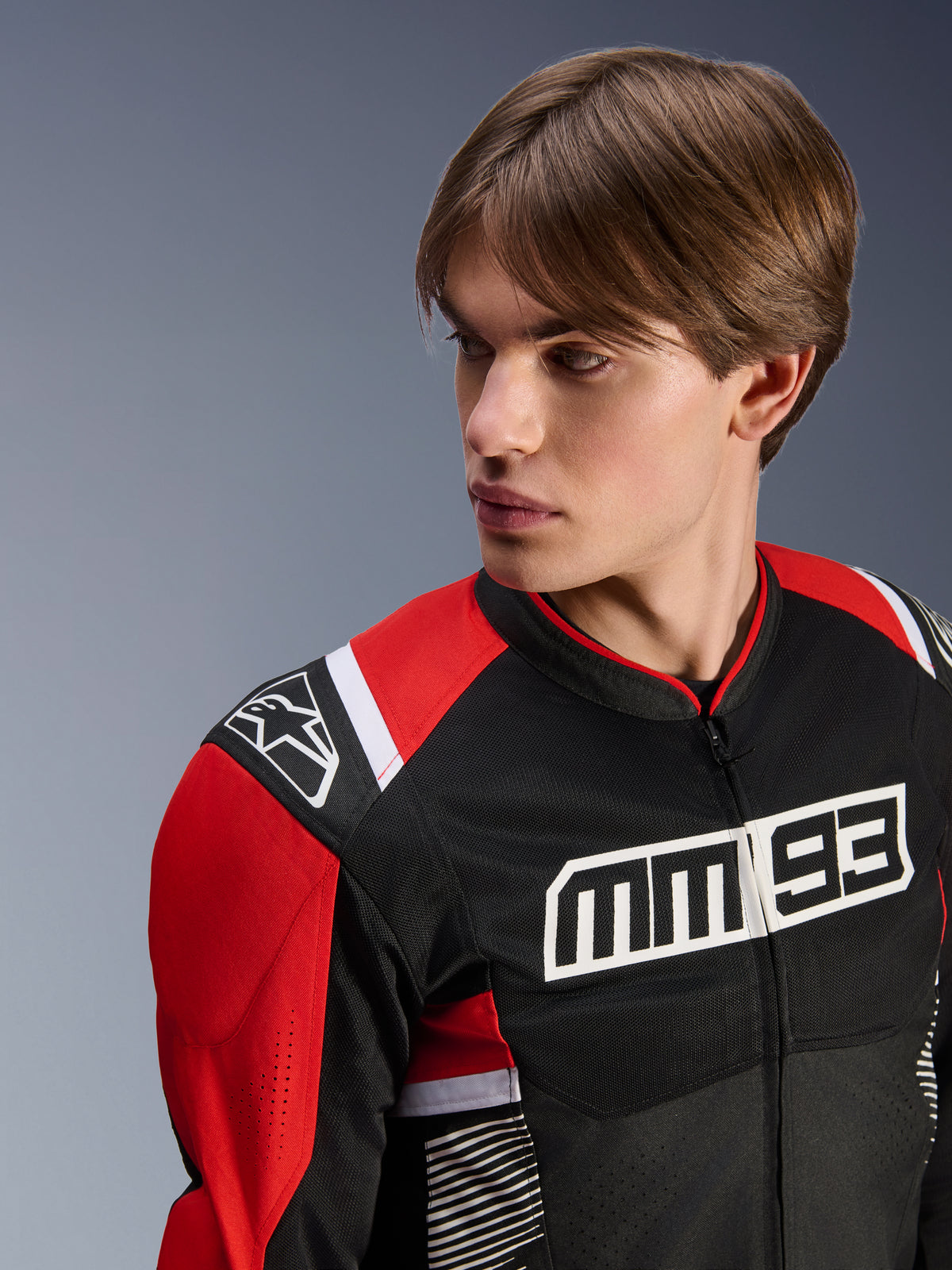 Męski model w kurtce Alpinestars MM93 T-SPS Air V2, tekstylna kurtka motocyklowa, czarna z jaskrawoczerwonymi i białymi elementami, z wyraźnym logo MM 93 na klatce piersiowej i logo gwiazdy na ramieniu, siateczkowa konstrukcja zapewniająca przepływ powietrza, sportowa odzież motocyklowa