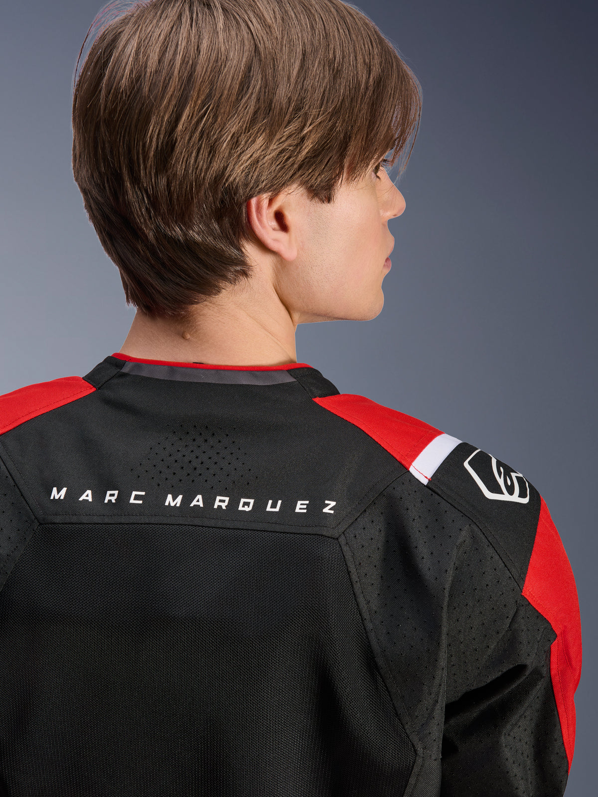 Kurtka Alpinestars MM93 T-SPS Air V2, widok z tyłu na górną część pleców i ramiona, czarna z jaskrawoczerwonymi i białymi detalami, napis „MARC MARQUEZ” na karczku, panele z siatki technicznej i logo na ramieniu, miejska sportowa odzież motocyklowa