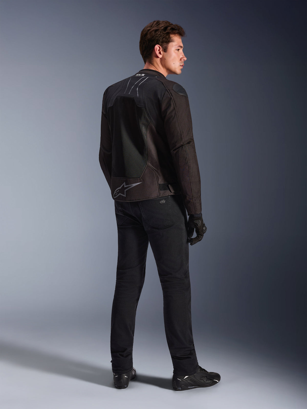 Kurtka motocyklowa Alpinestars SMX Air Black Anthracite, widok z tyłu na modelu, oznaczenie Tech-Air® Ready na kołnierzu i logo Astar w dolnej części pleców, czarne spodnie i buty motocyklowe