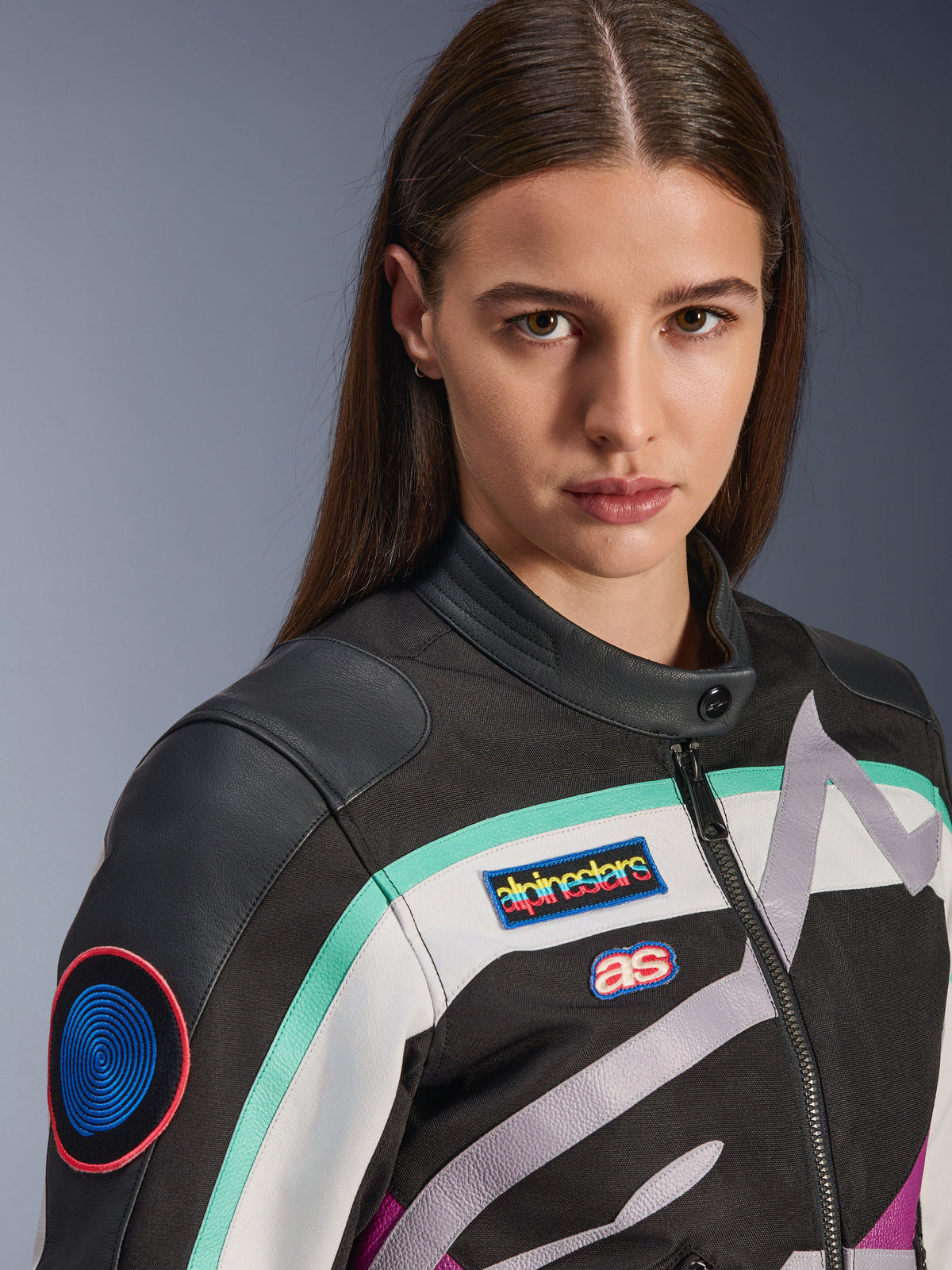 Alpinestars Idles Women's Jacket, damska kurtka motocyklowa, czarna, złamana biel i fioletowa z turkusowymi akcentami, zbliżenie na kolorowe naszywki Alpinestars heritage i detale na ramionach ze skóry koziej, design inspirowany stylem vintage do jazdy miejskiej