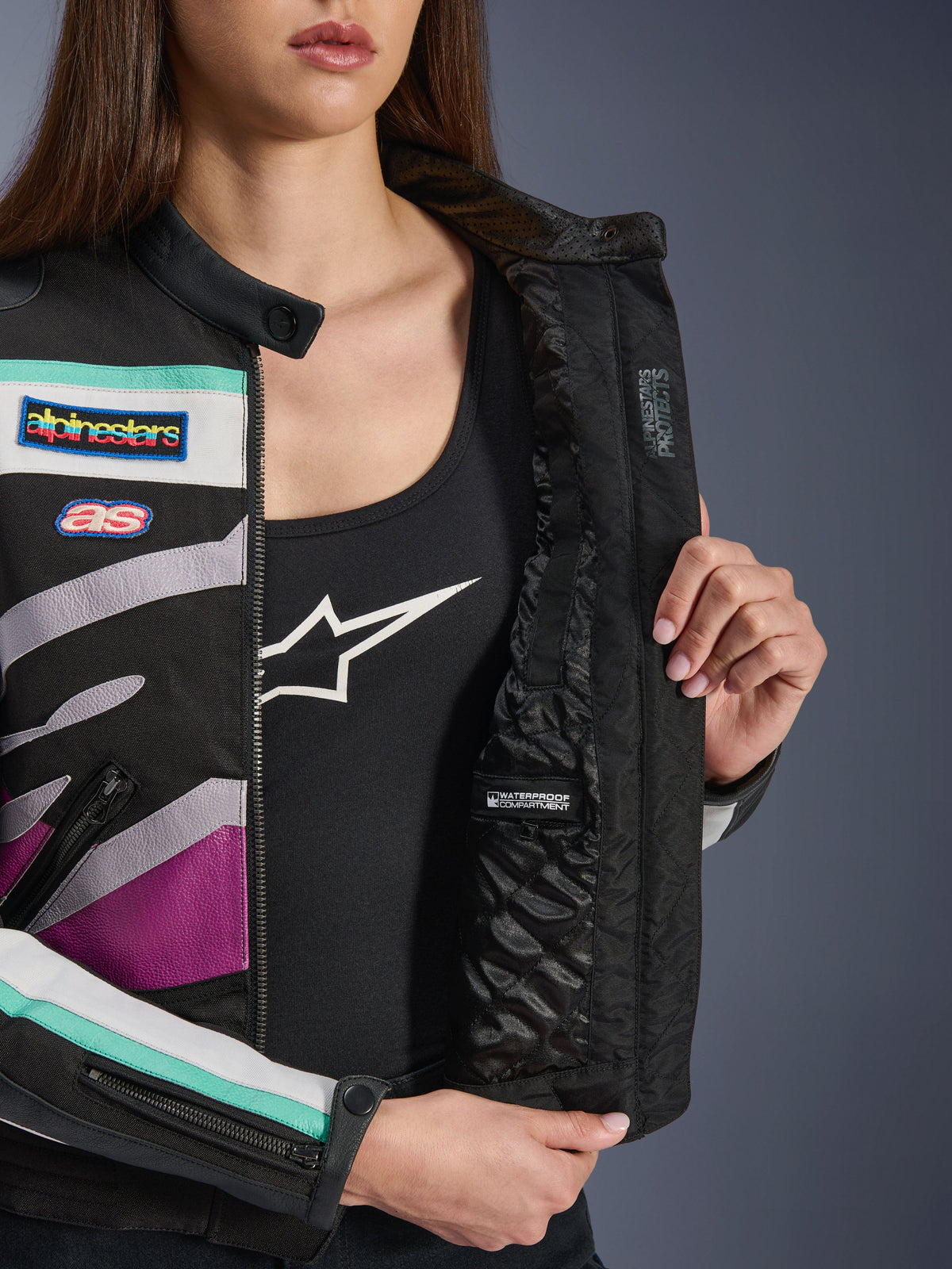 Damska kurtka Alpinestars Idles, Black Off White Purple, zbliżenie na wewnętrzną pikowaną podszewkę z wodoodporną przegrodą, wyścigowe naszywki w stylu vintage oraz morskie i fioletowe akcenty na tekstylnej warstwie zewnętrznej.