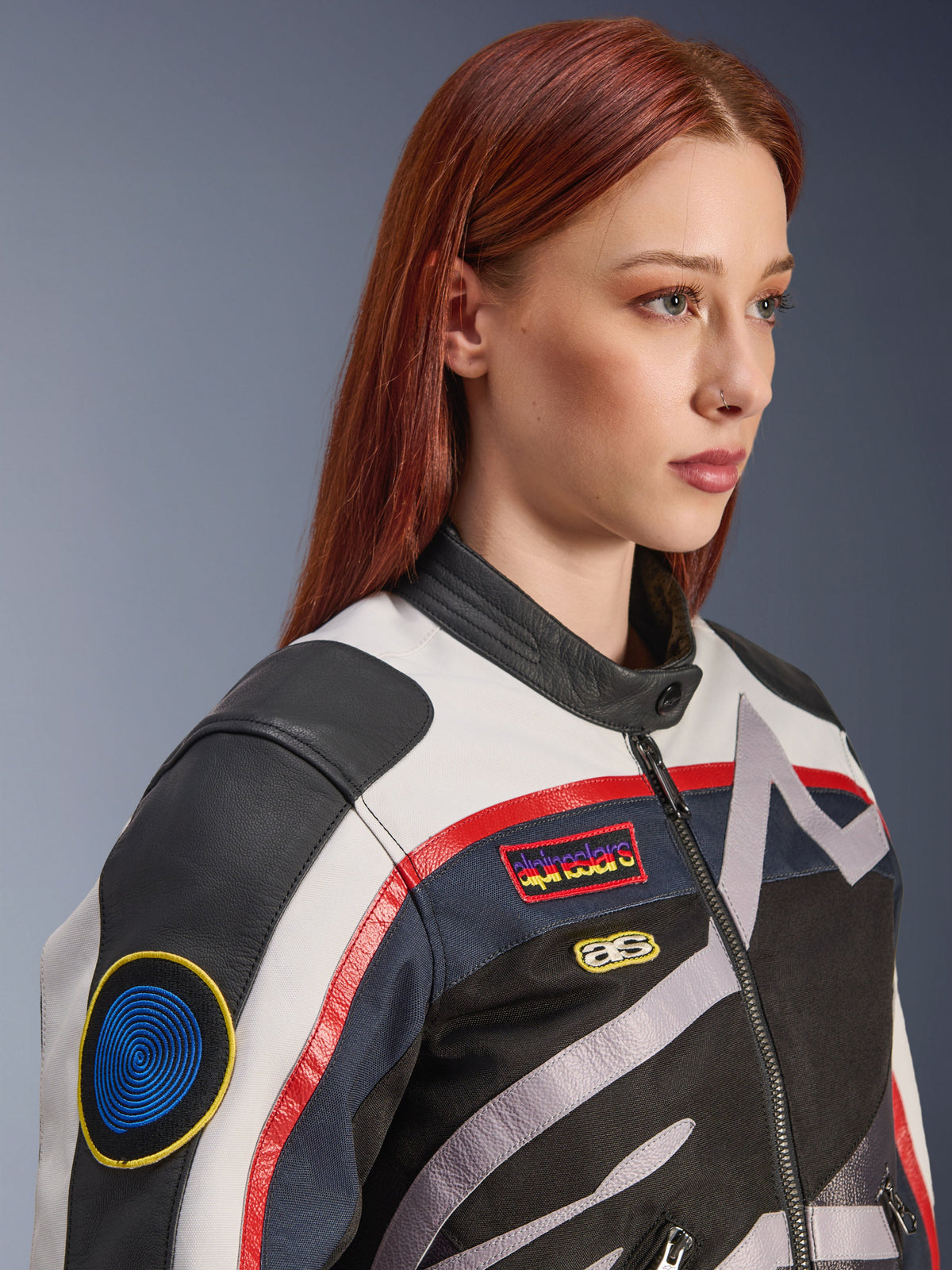Kurtka damska Alpinestars Idles, złamana biel, płomienna czerwień i czerń, naszywki wyścigowe w stylu vintage i logo oplatające kurtkę, konstrukcja tekstylno-skórzana, miejski styl motocyklowy, noszona przez modelkę.
