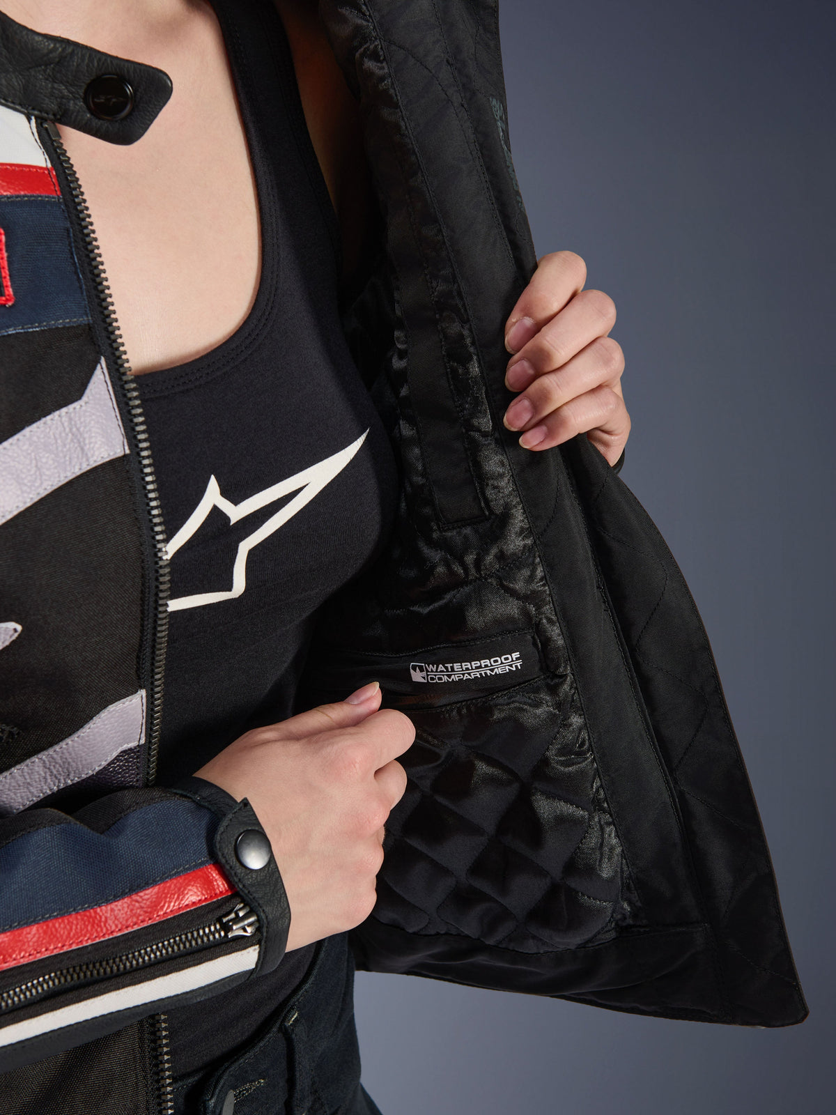 Damska kurtka Alpinestars Idles, detal wnętrza pokazujący czarną pikowaną podszewkę i oznakowaną wodoodporną przegrodę, noszona na czarnym topie z logo, funkcjonalna odzież motocyklowa dla kobiet