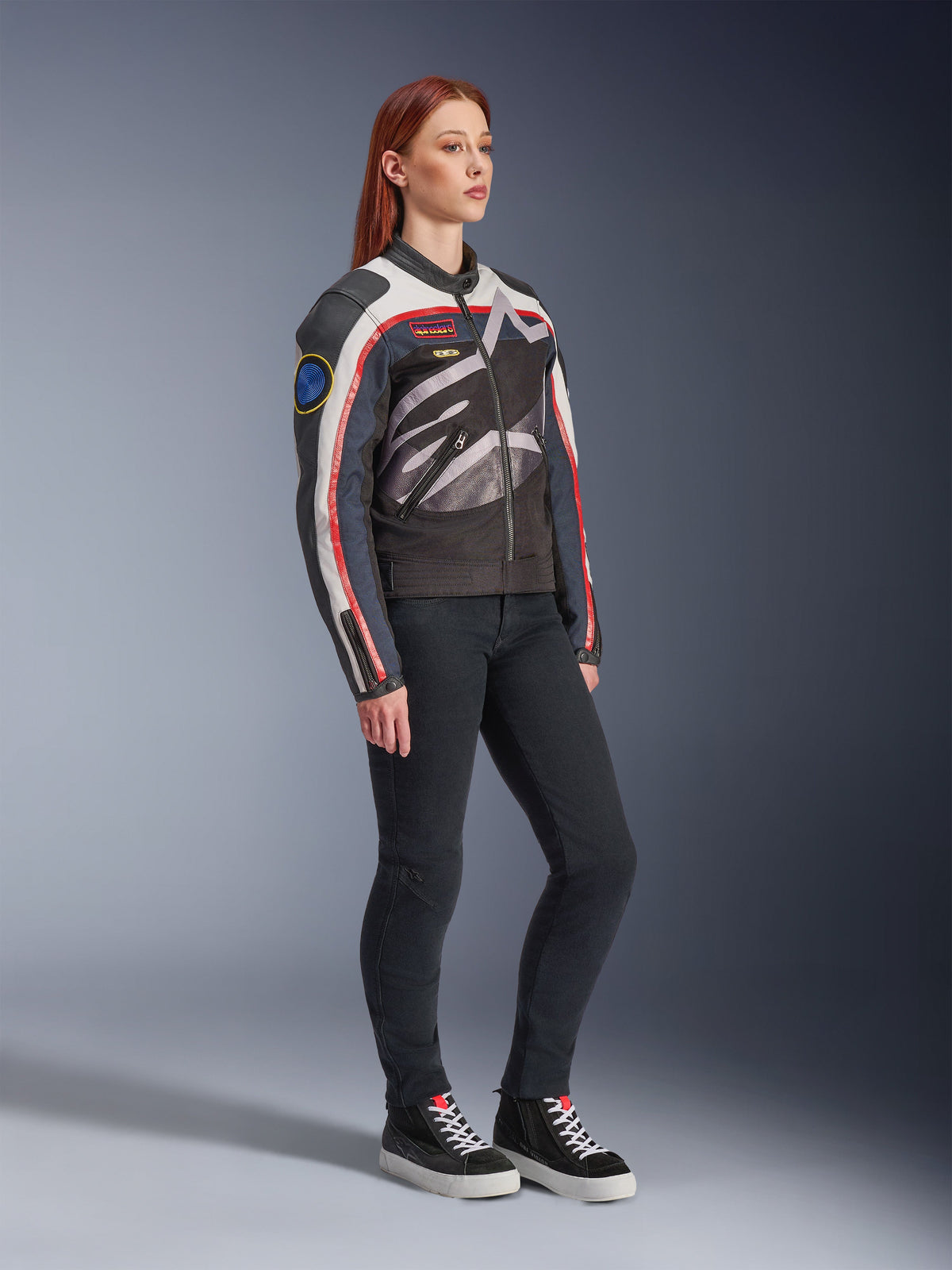 Kurtka damska Alpinestars Idles, kurtka motocyklowa, kremowy, jaskrawoczerwony i czarny, z dużym oplatającym logo Alpinestars i naszywkami inspirowanymi wyścigami retro, noszona z czarnymi spodniami i wysokimi trampkami, nowoczesna miejska odzież motocyklowa