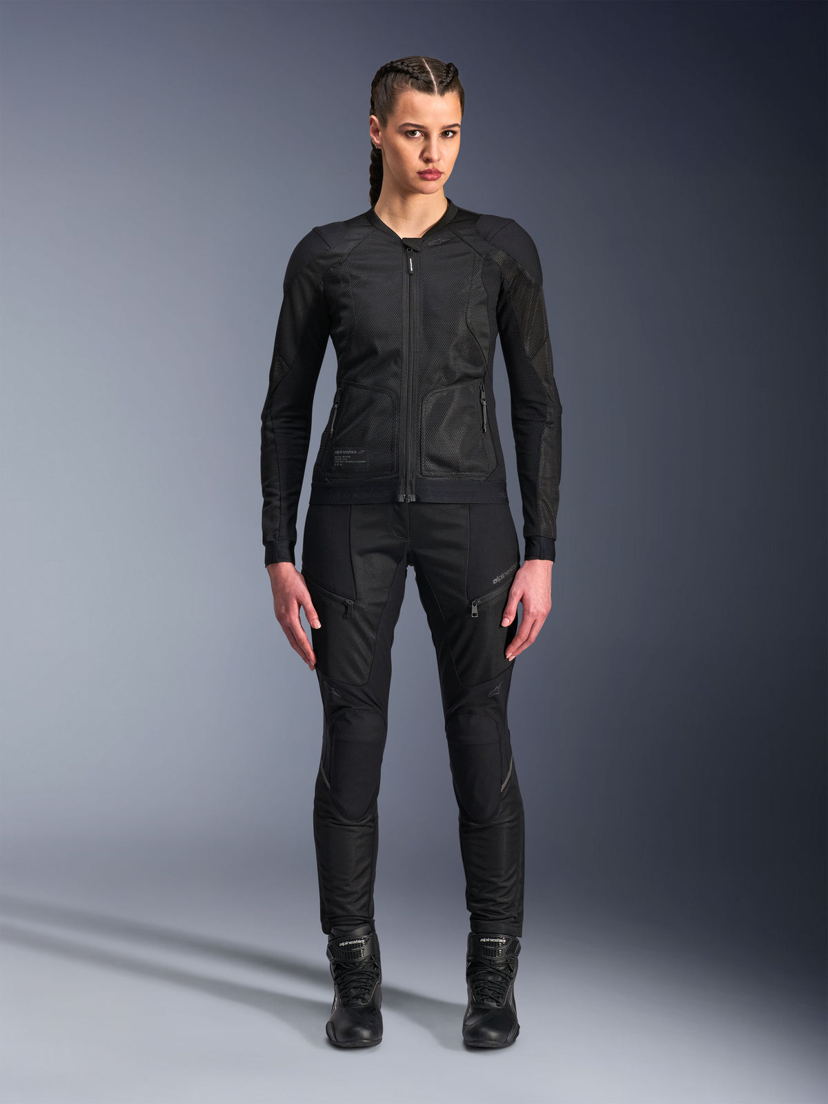Alpinestars Stella Troop-Air Jacket, damska kurtka motocyklowa, czarna, techniczna konstrukcja z siatki 2D o minimalistycznym designie, noszona z czarnymi spodniami i butami motocyklowymi, nowoczesny miejski styl motocyklowy