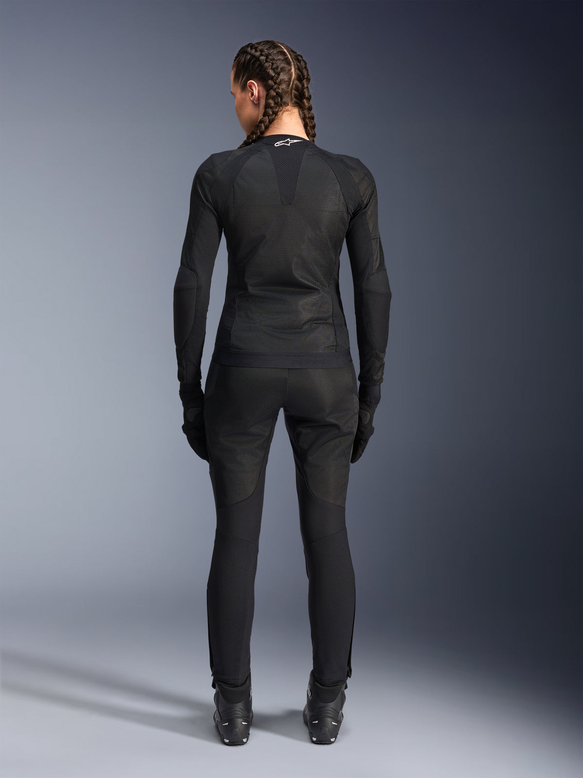 Alpinestars Stella Troop-Air Jacket, damska kurtka motocyklowa, czarna, widok z tyłu motocyklistki ubranej w techniczną kurtkę z siatki, zestawioną z pasującymi czarnymi spodniami motocyklowymi, rękawicami i butami, dopasowany, oddychający design z białym logo Alpinestars na kołnierzu