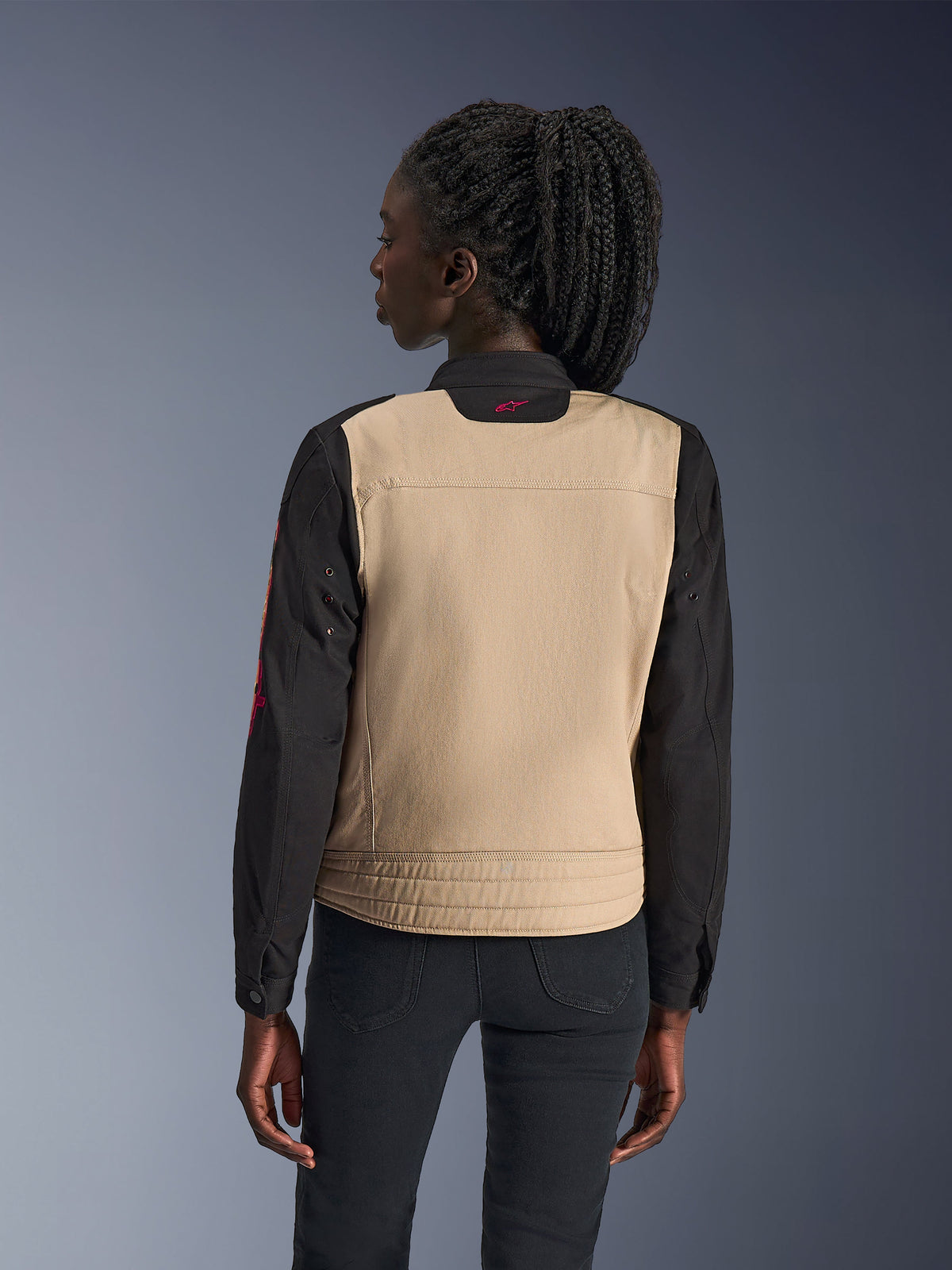 Alpinestars Woman Stella Grace Jacket, miejska kurtka motocyklowa, kolor aluminiowy i czarny, widok z tyłu ukazujący beżowy panel na plecach i czarne rękawy, design inspirowany odzieżą roboczą z małym różowym logo na kołnierzu, zestawiona z ciemnymi spodniami