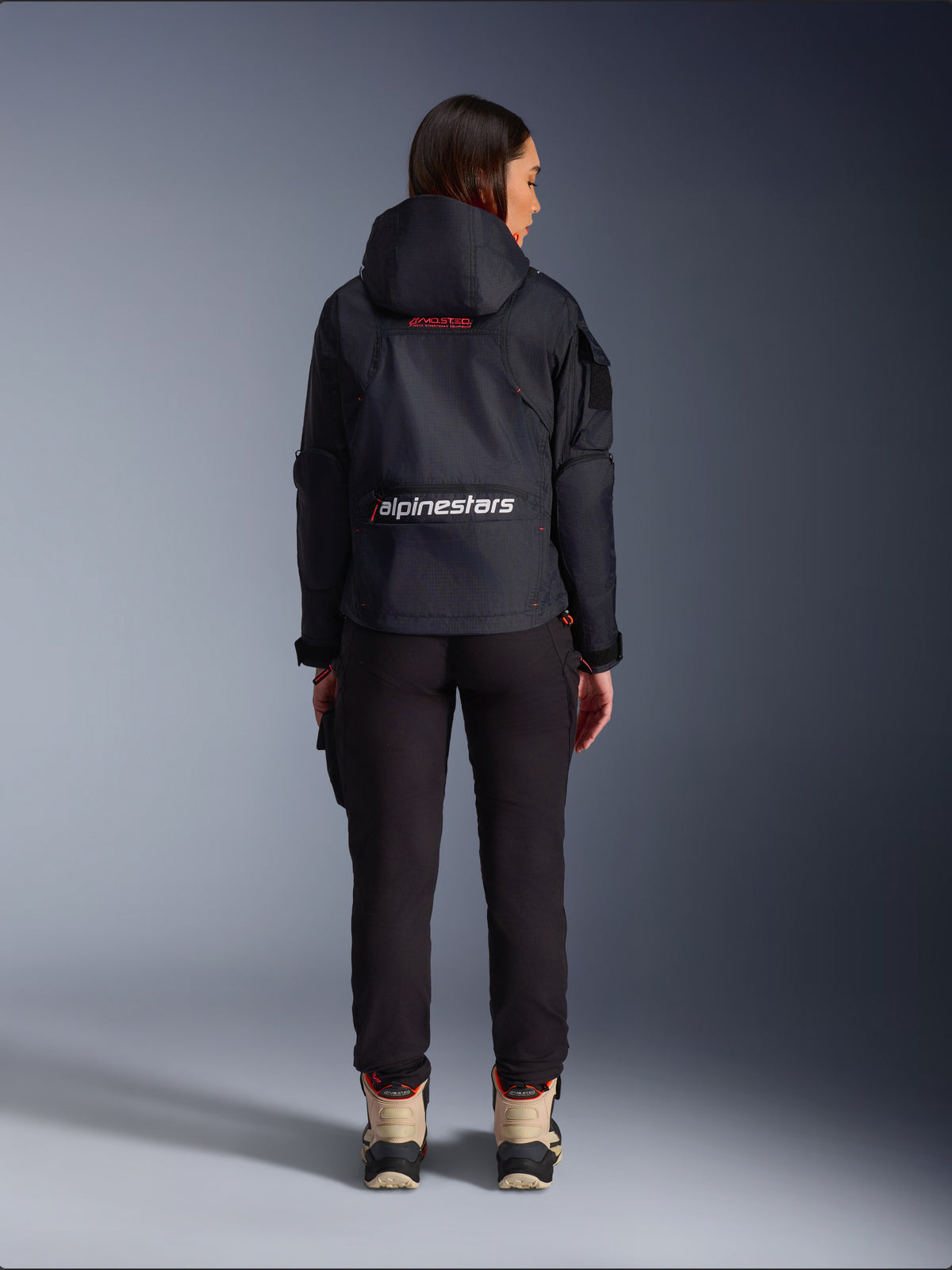 Alpinestars Molly Air Jacket, Urban Motorcycle Jacket, Black and Fluo Coral, back view featuring a hood and large white branding on the lower back, worn with black pants and tan riding boots, lightweight textile construction