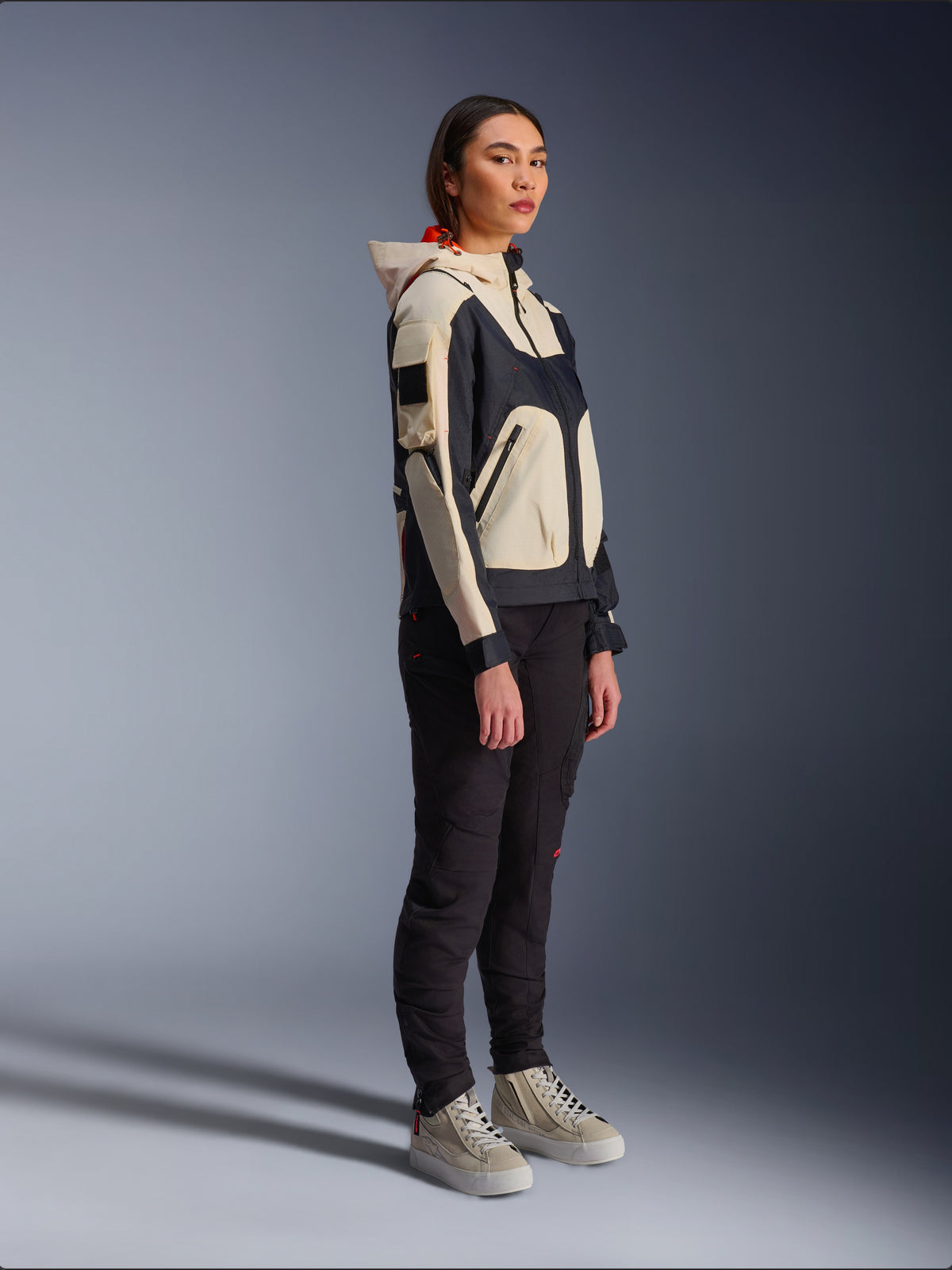 Kurtka Alpinestars Molly Air Jacket w kolorze Black Almond, noszona przez motocyklistkę z czarnymi spodniami i kremowymi wysokimi sneakersami, charakteryzująca się dwukolorowym designem z czarnymi i beżowymi panelami, zintegrowanym kapturem i nowoczesnym stylem miejskim.