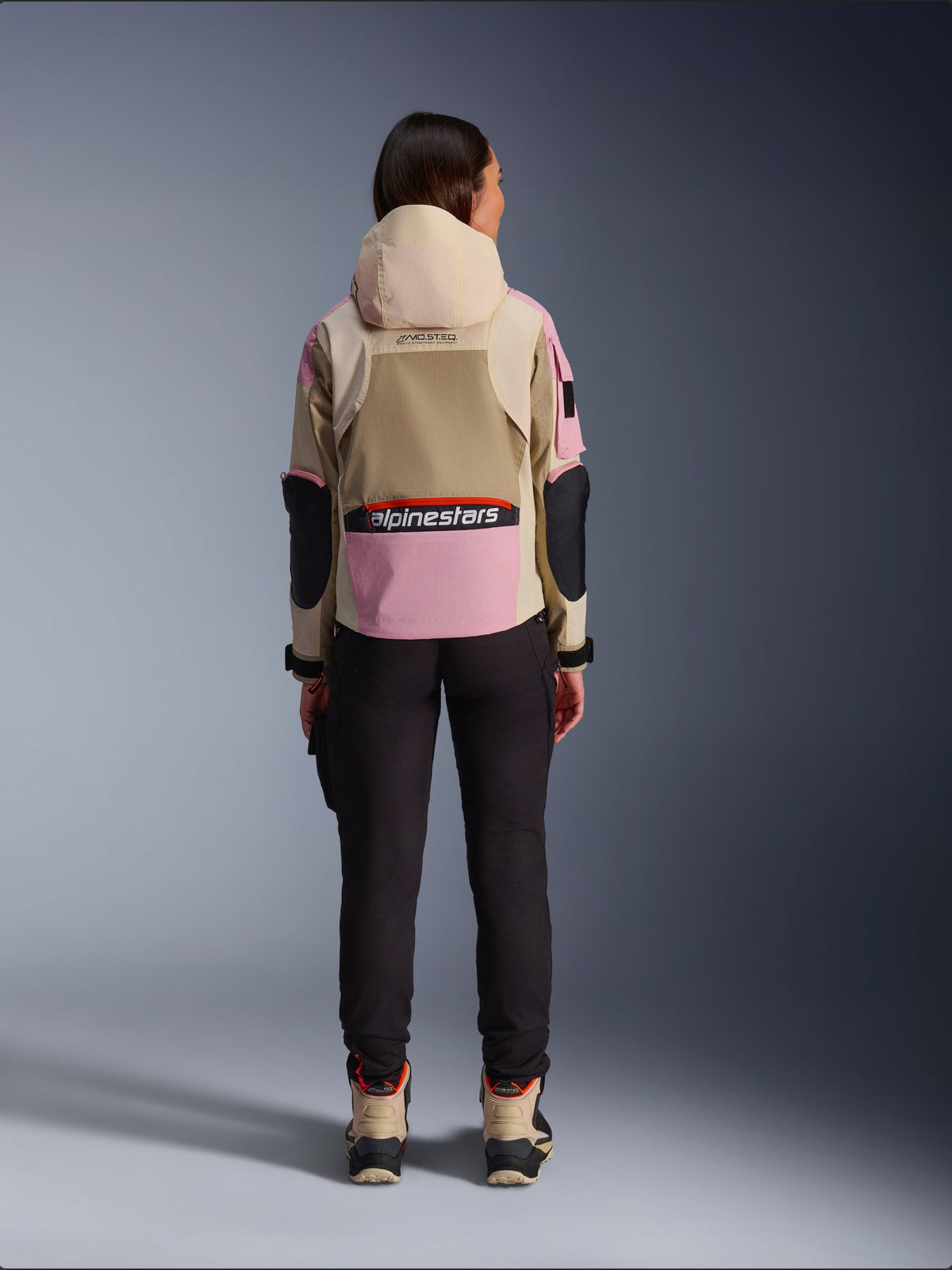Alpinestars Molly Air Jacket, damska kurtka motocyklowa widziana od tyłu, kolor Sand Pink Almond, beżowy kaptur i różowe panele z czarnymi akcentami, czarne spodnie i beżowe buty motocyklowe, współczesna miejska odzież motocyklowa