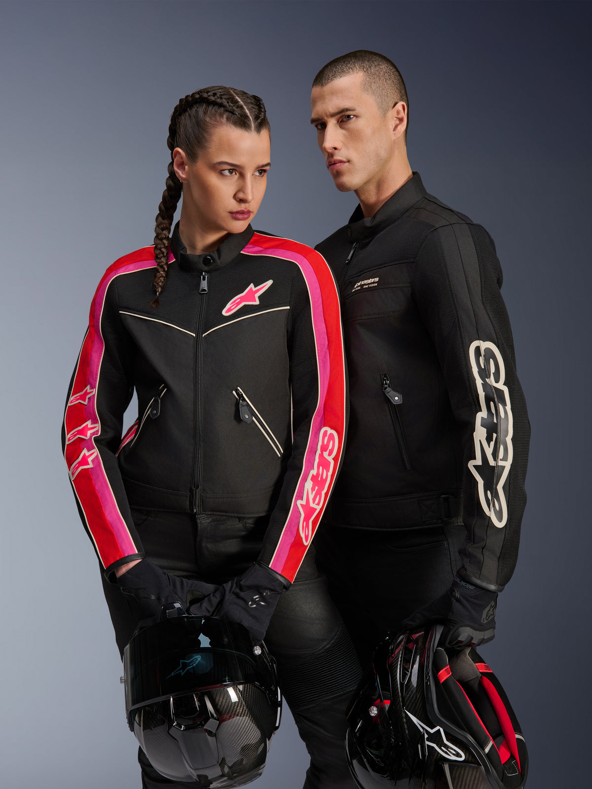 Alpinestars Stella T-Dyno Air Jacket na kobiecie w kolorze czarnym, jaskrawoczerwonym i fuksji, w zestawieniu z męską czarną kurtką Dyno Air Jacket, oboje motocykliści trzymają kaski motocyklowe, ujęcie studyjne współczesnej miejskiej odzieży motocyklowej