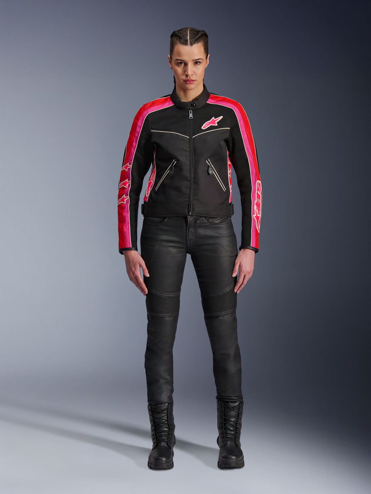 Motocyklistka w kurtce Alpinestars Stella T-Dyno Air, czarna z jaskrawoczerwonymi i fuksjowymi akcentami, zestawiona z czarnymi spodniami motocyklowymi i sznurowanymi butami, panele z siatki 3D, dopasowany krój, różowe logo gwiazdy, miejski strój motocyklowy