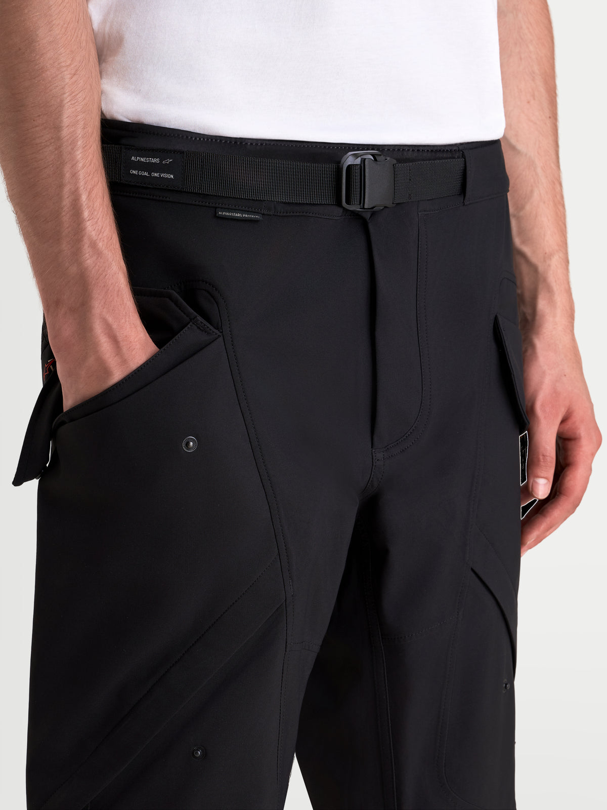 Alpinestars Juggernaut V2 Drystar spodnie motocyklowe miejskie męskie, czarne, zbliżenie na regulowany pasek z klamrą magnetyczną i boczne kieszenie typu cargo na modelu