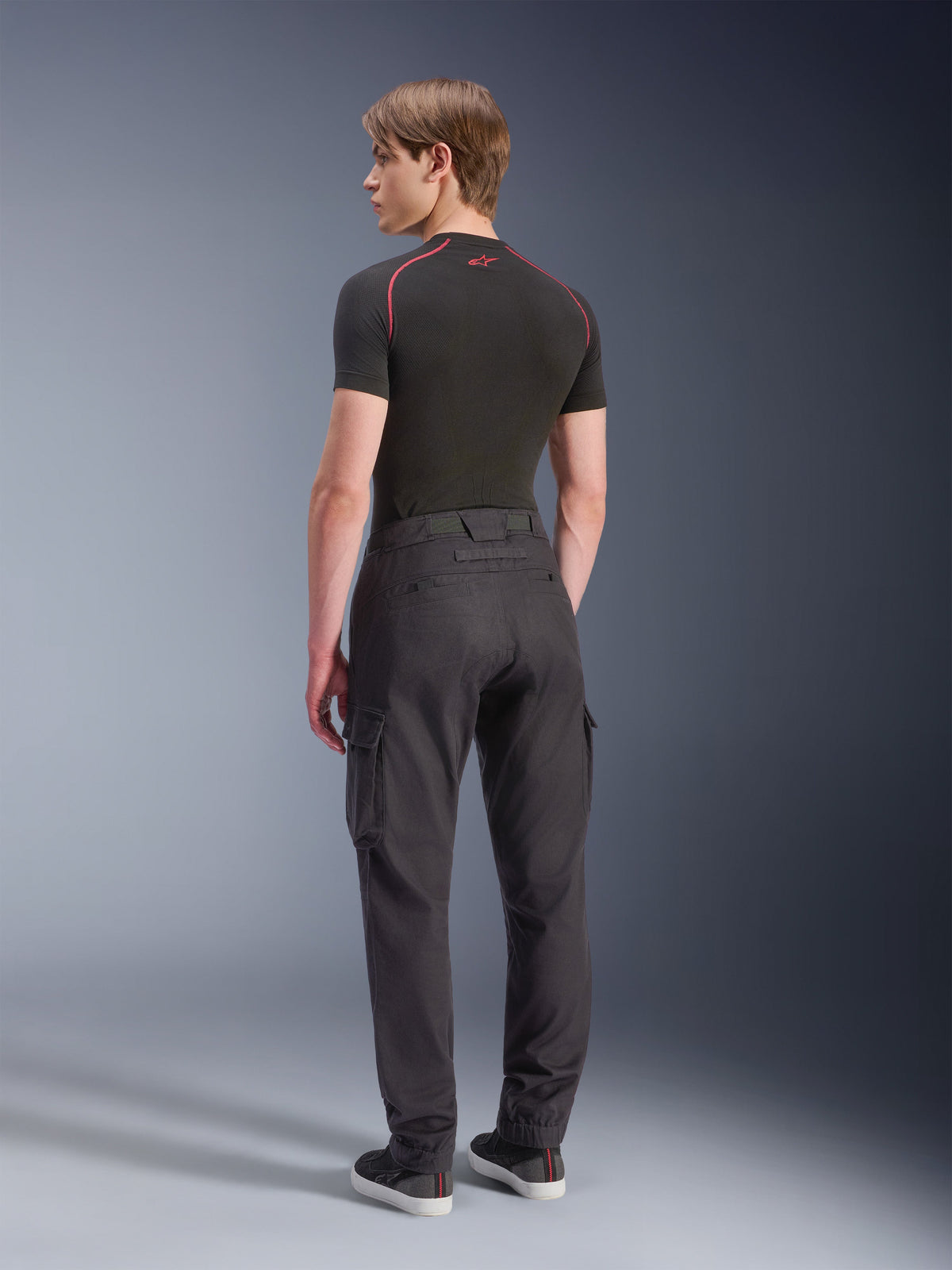 Alpinestars Flex-AST Cargo Pants - Short, motocyklowe spodnie cargo, czarne, widok z tyłu na modela w spodniach cargo o regularnym, zwężanym kroju z bocznymi kieszeniami i elastycznymi mankietami, w zestawieniu z czarną warstwą bazową i butami casualowymi