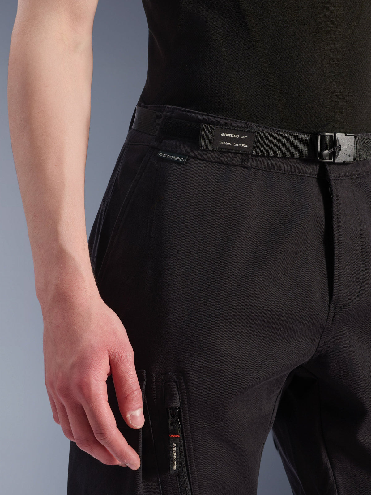 Alpinestars Flex-AST Cargo Pants, miejskie spodnie motocyklowe, czarne, widok z bliska na talię i boczną kieszeń, zintegrowany pasek z logo Alpinestars, zapięcie na klamrę, kieszeń na zamek z markowym uchwytem, techniczna konstrukcja tekstylna do jazdy miejskiej