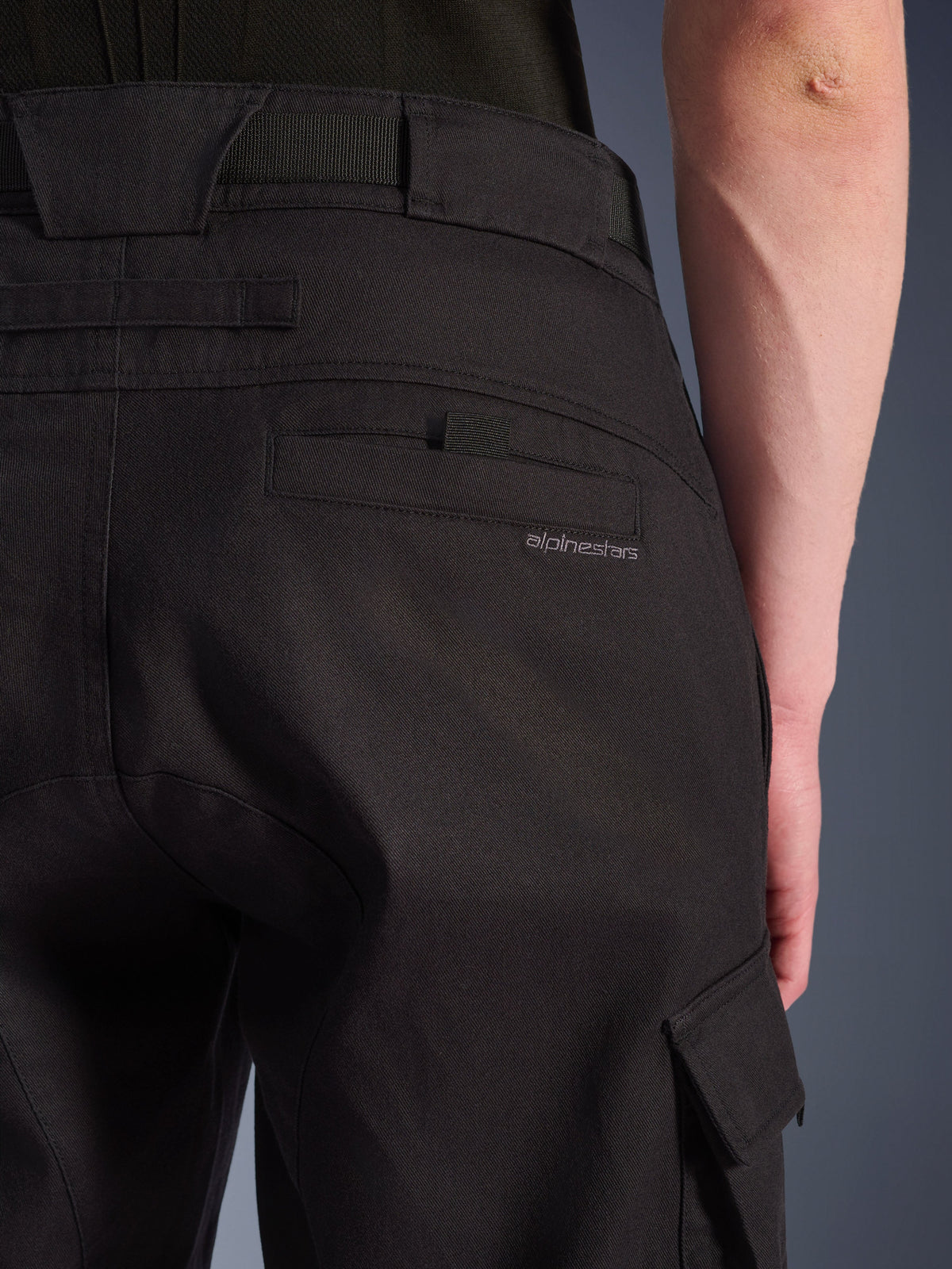 Zbliżenie na spodnie Alpinestars Flex-AST Cargo w kolorze czarnym, miejskie spodnie motocyklowe z detalami tylnej kieszeni i subtelnym brandingiem, dużymi szlufkami oraz boczną kieszenią cargo na wytrzymałej, elastycznej tkaninie.