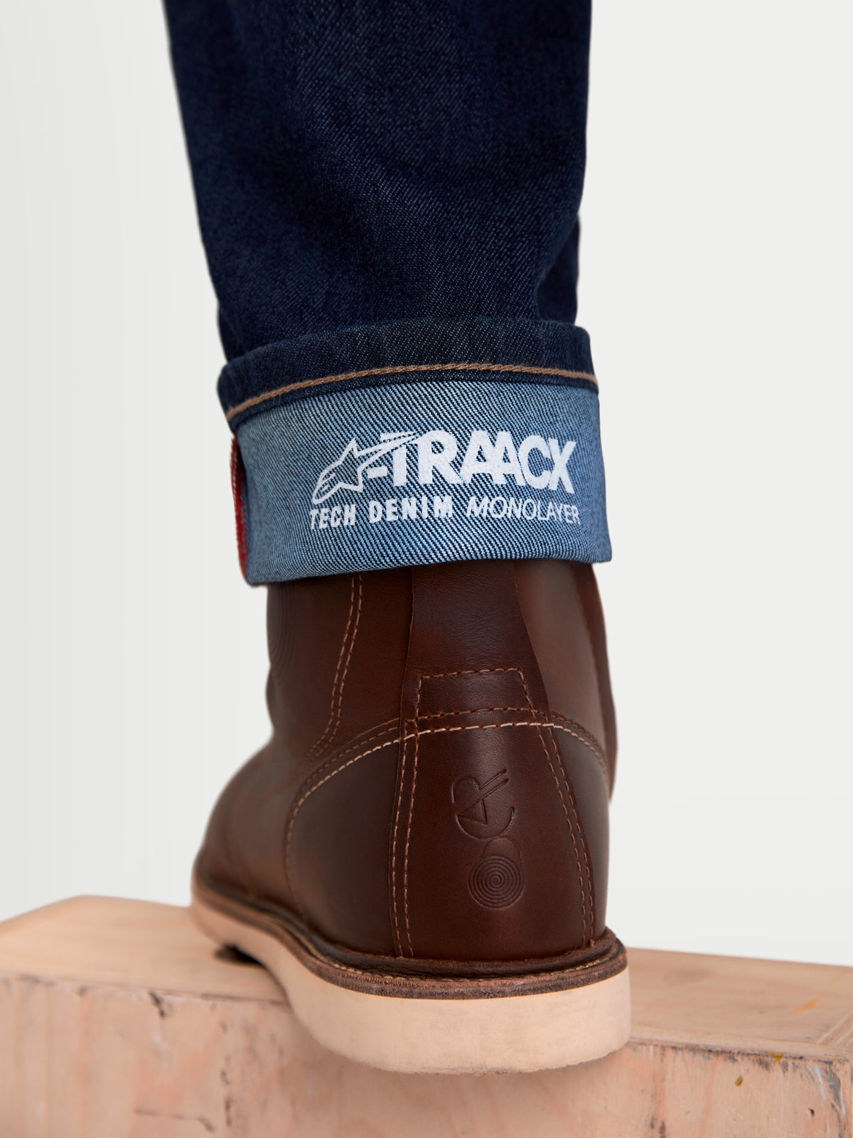 Alpinestars Flex Ast 7 Denim, męskie spodnie motocyklowe jeansy urban, ciemnoniebieskie, widok zbliżenia na wywinięty dół nogawki z brandingiem technicznego denimu A-TRAACX i brązowe skórzane buty
