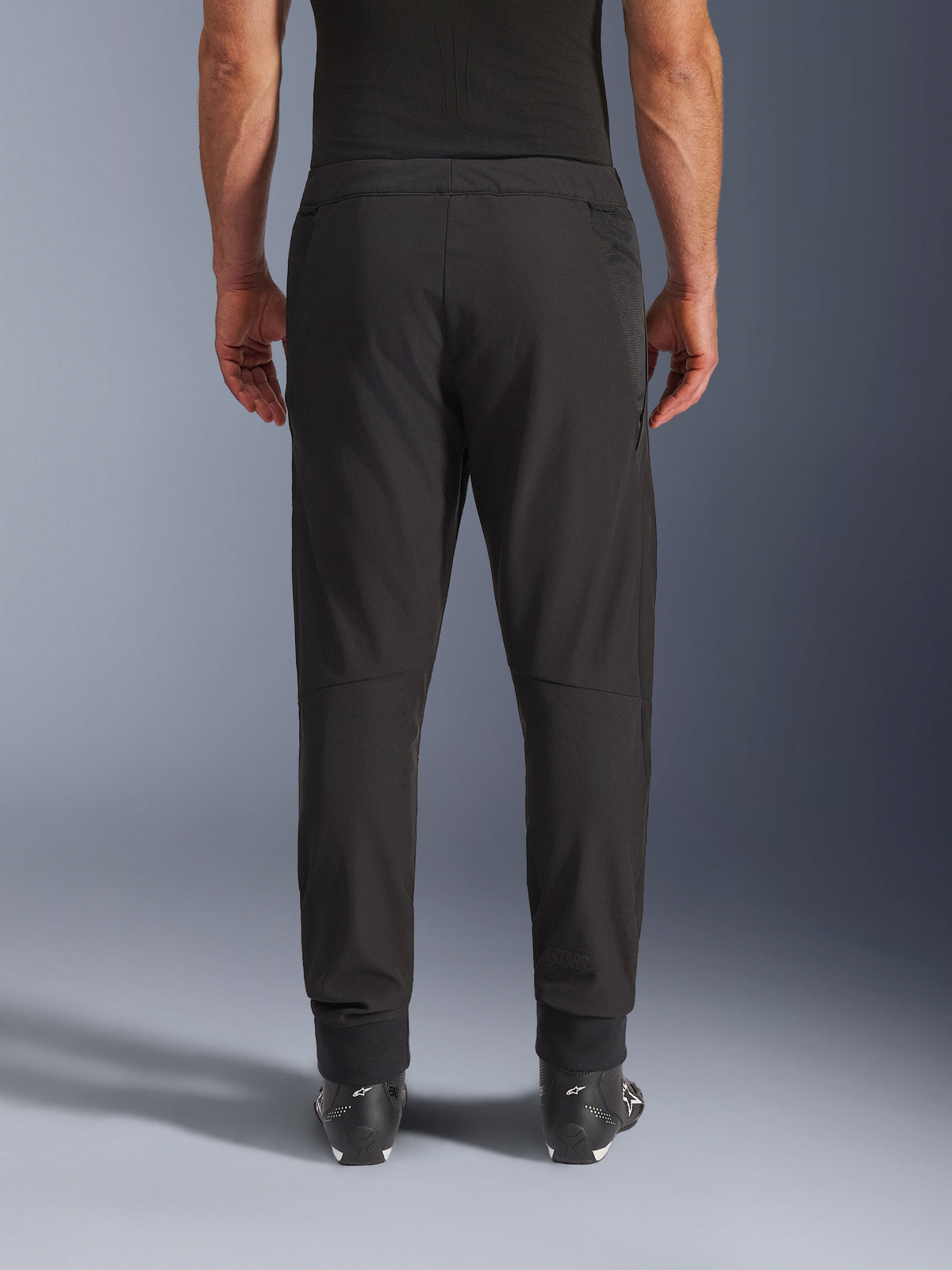 Alpinestars Aeroshell Airflow Pants, Black, rear view, featuring laser-perforated zones on the calves and mesh paneling, worn with black Alpinestars boots, lightweight softshell design for sport and touring