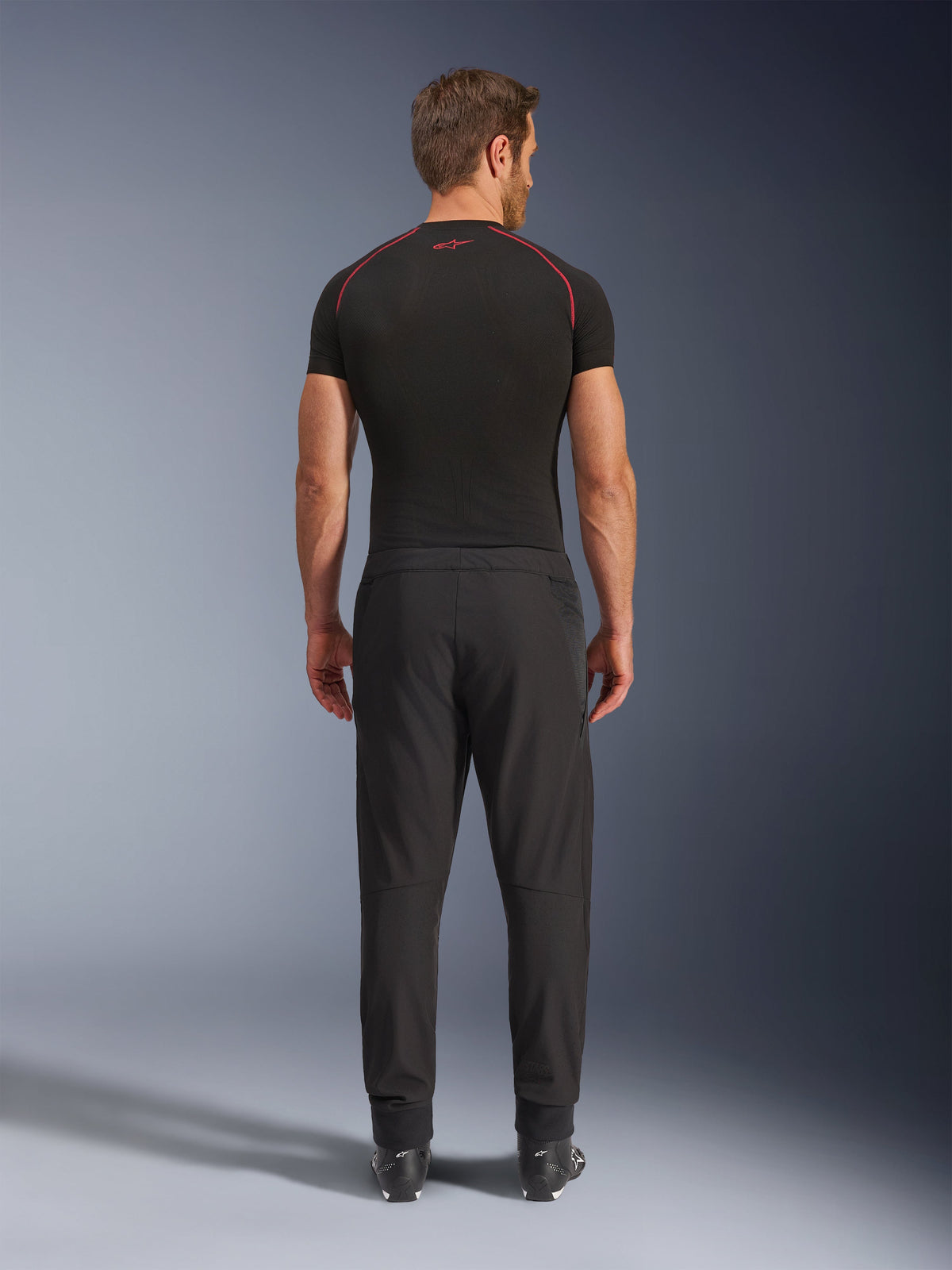 Alpinestars Aeroshell Airflow Pants, Black Motorcycle Pants, back view shown on a model with a black base layer and boots, featuring a lightweight softshell chassis with integrated mesh panels for ventilation.