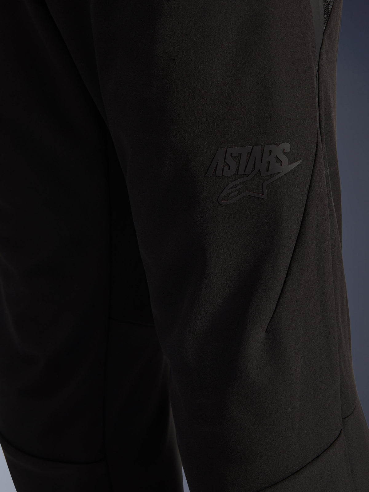 Alpinestars Aeroshell Airflow Pants, Black Motorcycle Pants, close-up view of the thigh area featuring a raised black ASTARS logo, lightweight stretch softshell material with ergonomic seam design