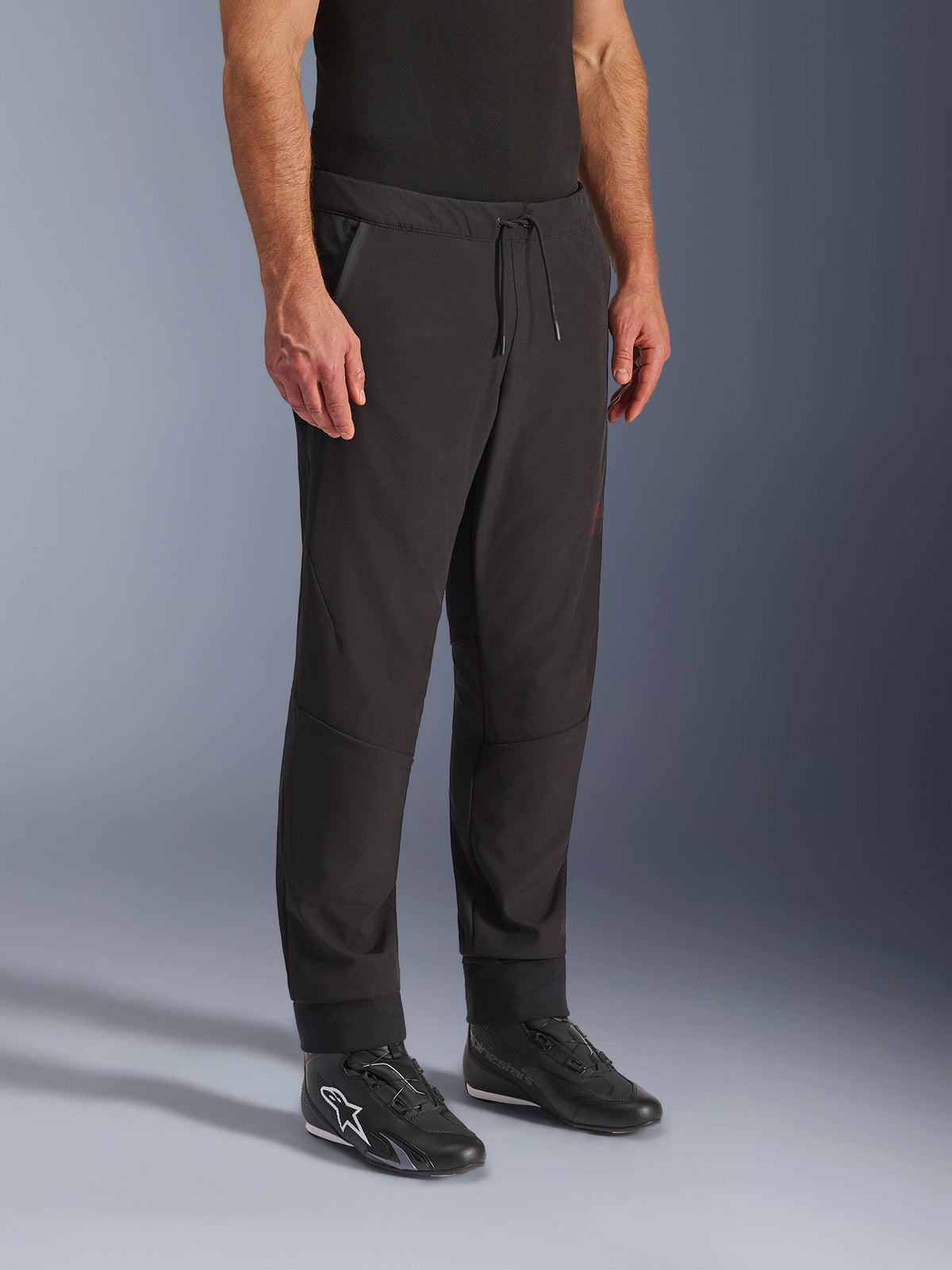 Alpinestars Aeroshell Airflow Pants, Black Motorcycle Pants, worn by model with black riding shoes, featuring a drawstring waistband, cuffed ankles, and laser-perforated softshell fabric for maximum ventilation
