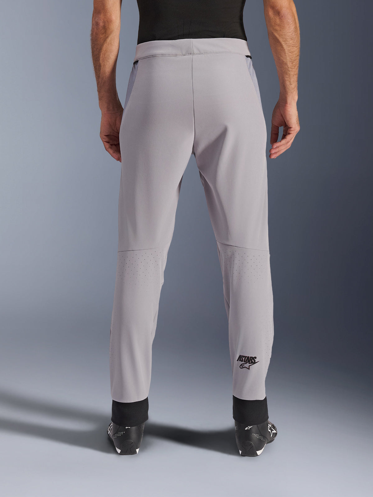 Alpinestars Aeroshell Airflow Pants, spodnie motocyklowe, Mid Gray, widok od tyłu ukazujący laserowo perforowane strefy na łydkach i czarne logo Astars, tekstylna konstrukcja softshell z czarnymi mankietami na kostkach i siatkowymi panelami na biodrach.