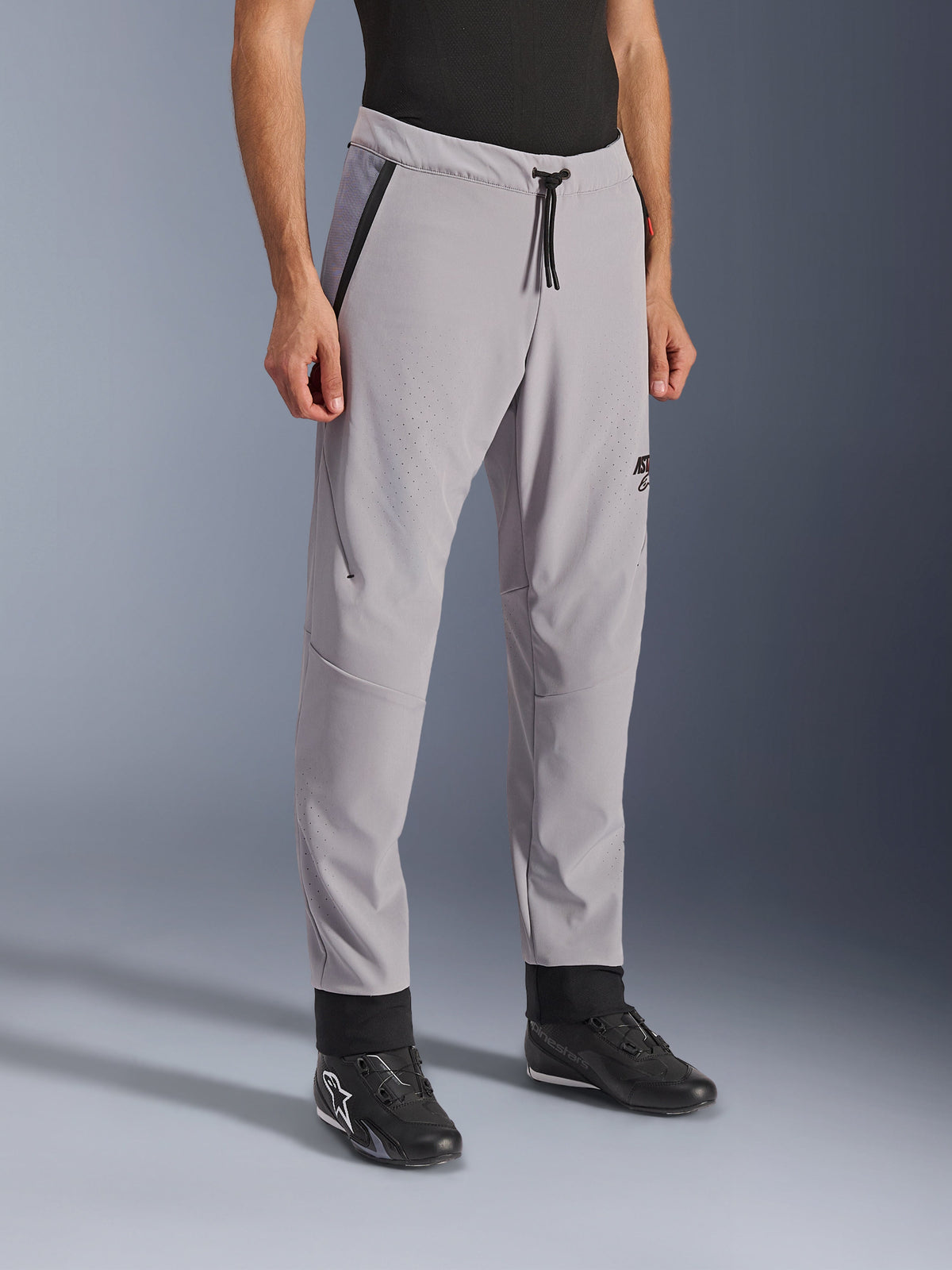 Alpinestars Aeroshell Airflow Pants, Mid Gray, lekkie spodnie motocyklowe z laserowo perforowanymi strefami wentylacyjnymi na udach i goleniach, z elastycznym pasem regulowanym sznurkiem i dopasowanym sportowym krojem, zaprezentowane na modelu w czarnych butach motocyklowych.