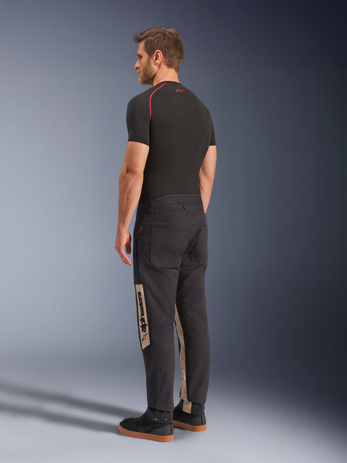 Alpinestars Flex-AST Canvas Pants, Black Aluminum, Urban Motorcycle Pants, featuring tan side panels with Alpinestars branding, worn with a black base layer and sneakers, back view showing workwear-inspired styling and ergonomic moto fit.