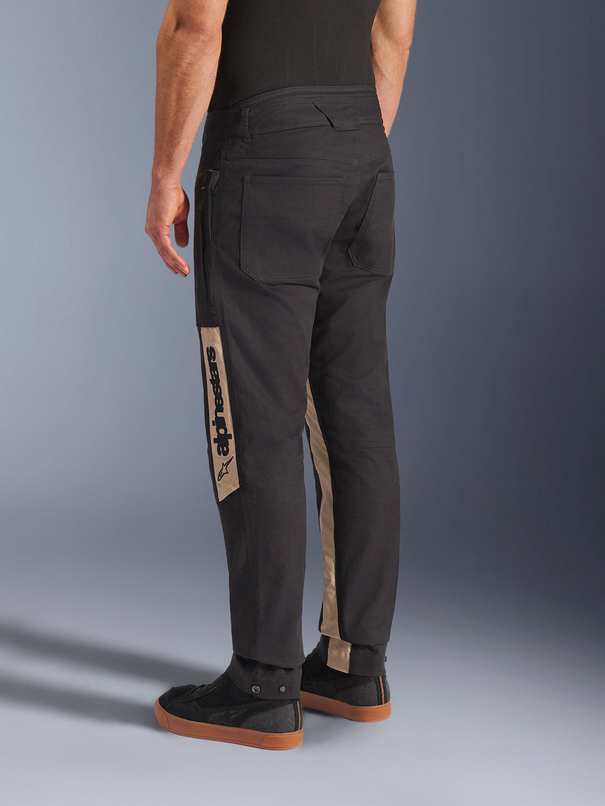 Alpinestars Flex-AST Canvas Pants in Black Aluminum, back view showing urban motorcycle trousers with large workwear-inspired pockets and tan vertical leg panels featuring Alpinestars branding.