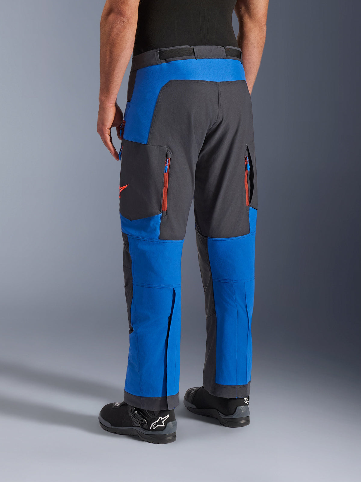 Alpinestars Maxdura Dual Pants, niebieskie i ciemnoszare, widok z tyłu przedstawiający kieszenie na zamek i strefy wentylacyjne, krój na buty noszony z czarnymi butami Alpinestars, wytrzymała odzież do jazdy adventure i dual-sport